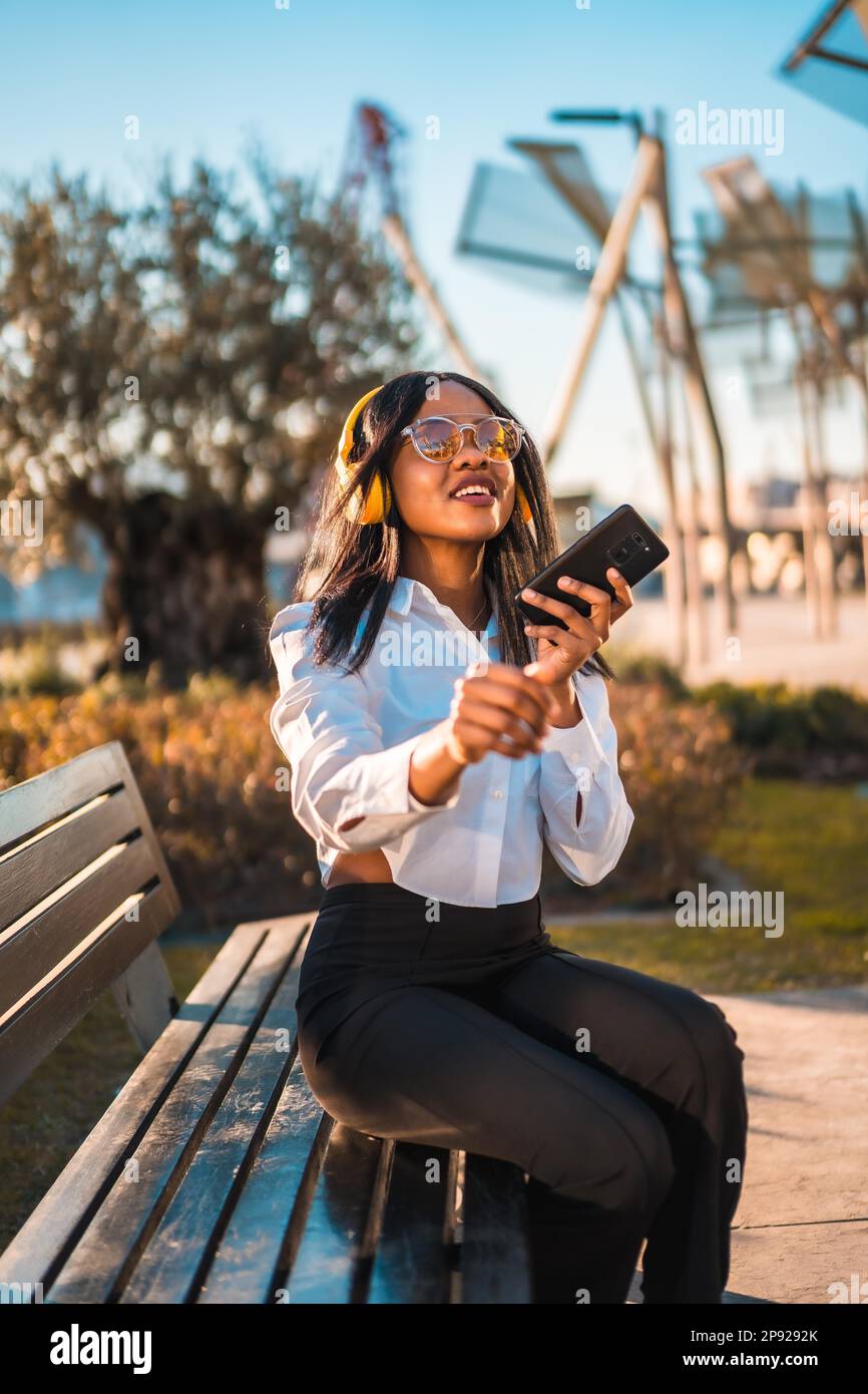 African american woman listening to music with headphones at sunset in a park, dancing smiling Stock Photo