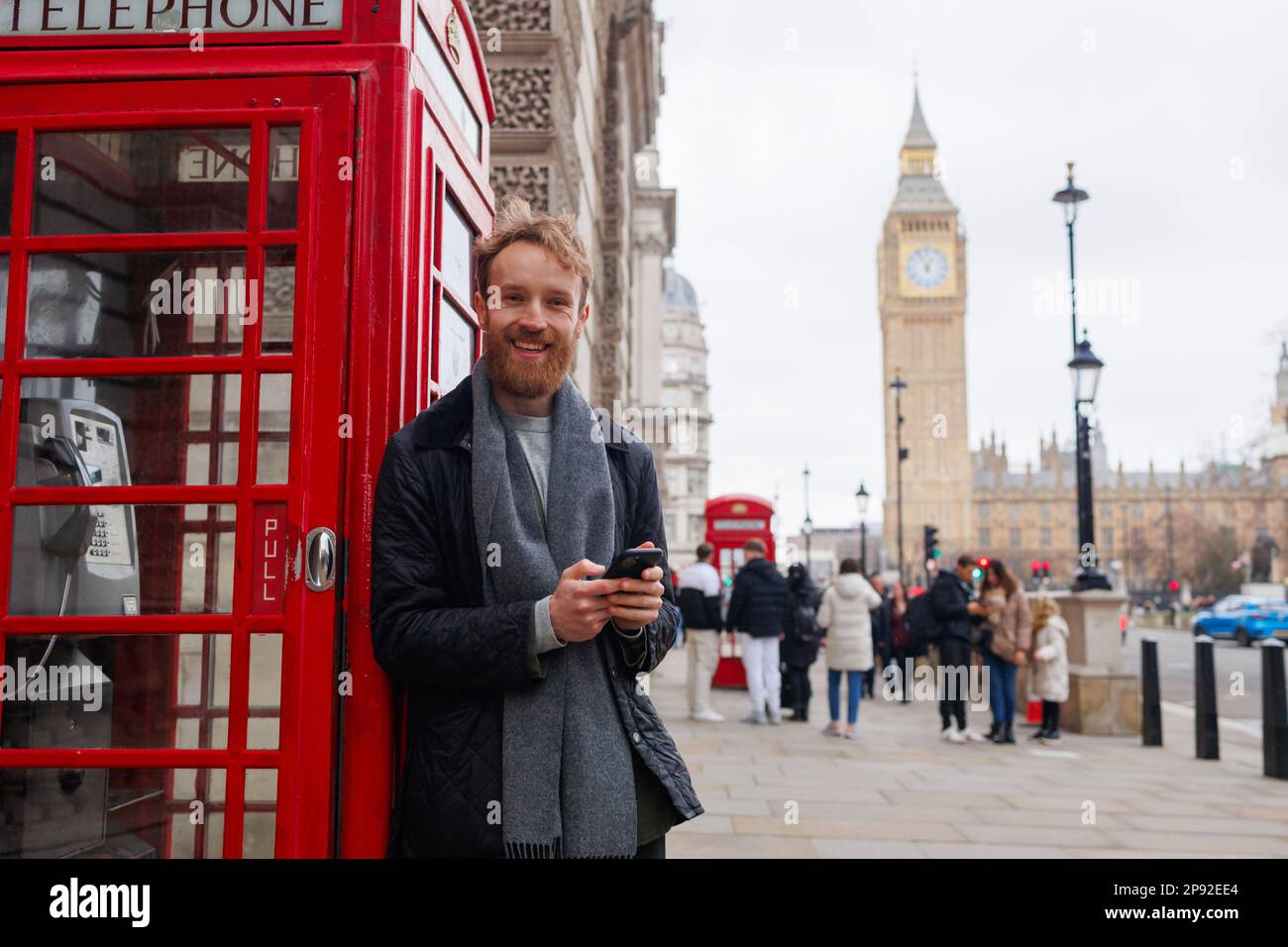 Man Using Red Telephone Smiling man with a smartphone in his hands stands near the famous red ...