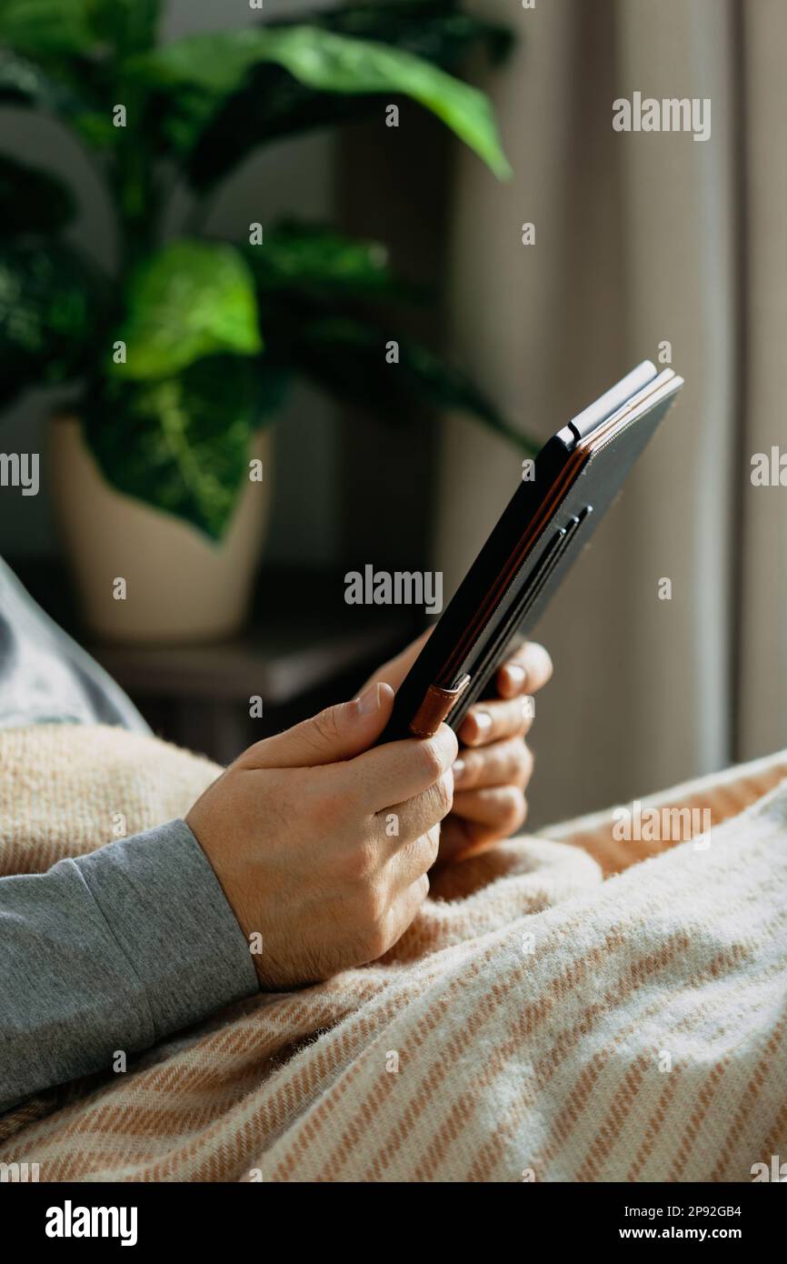 a caucasian man relaxing, using digital tablet lying in bed under throw at home Stock Photo
