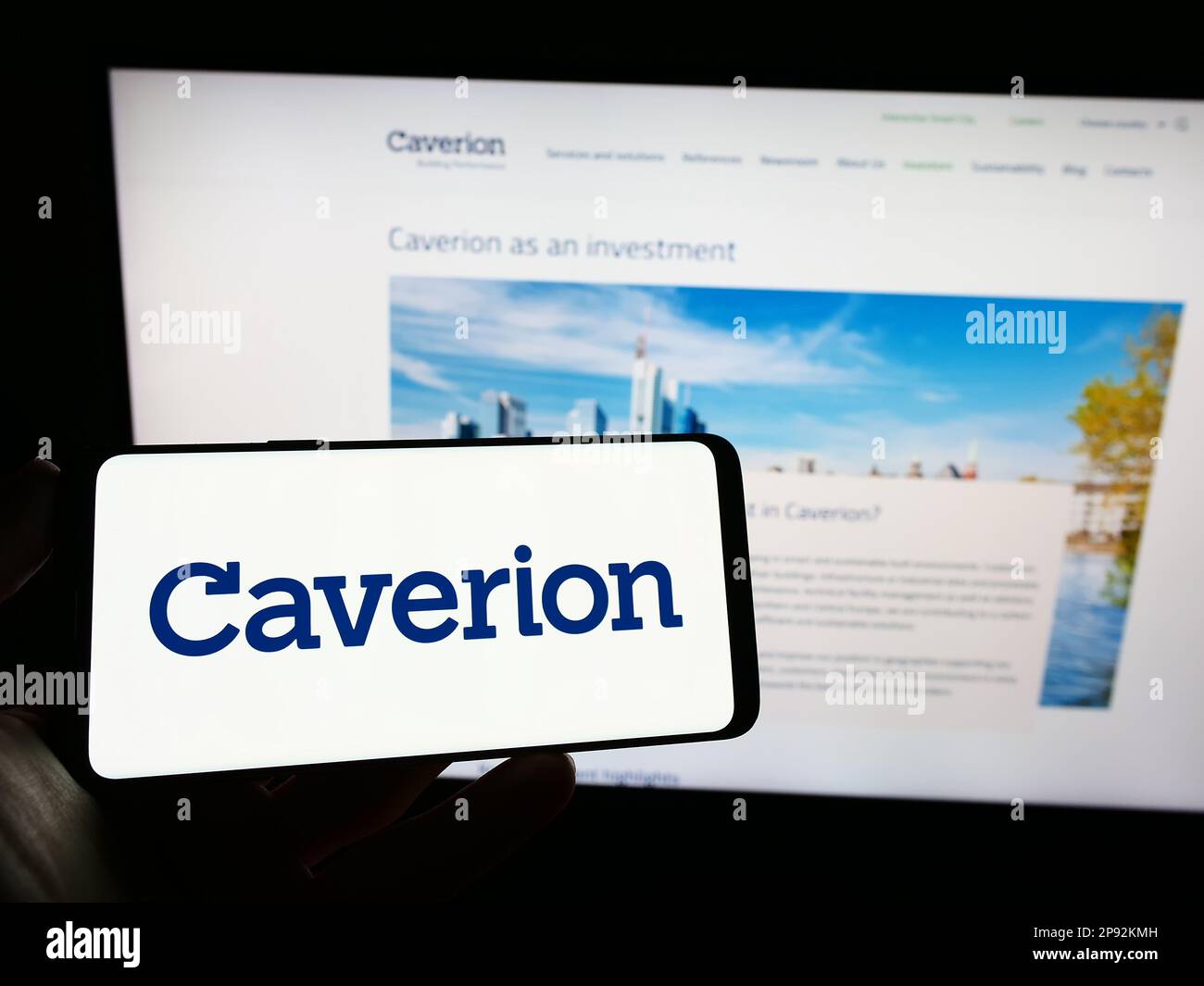 Person holding mobile phone with logo of building technology company Caverion Oyj on screen in front of business web page. Focus on phone display. Stock Photo