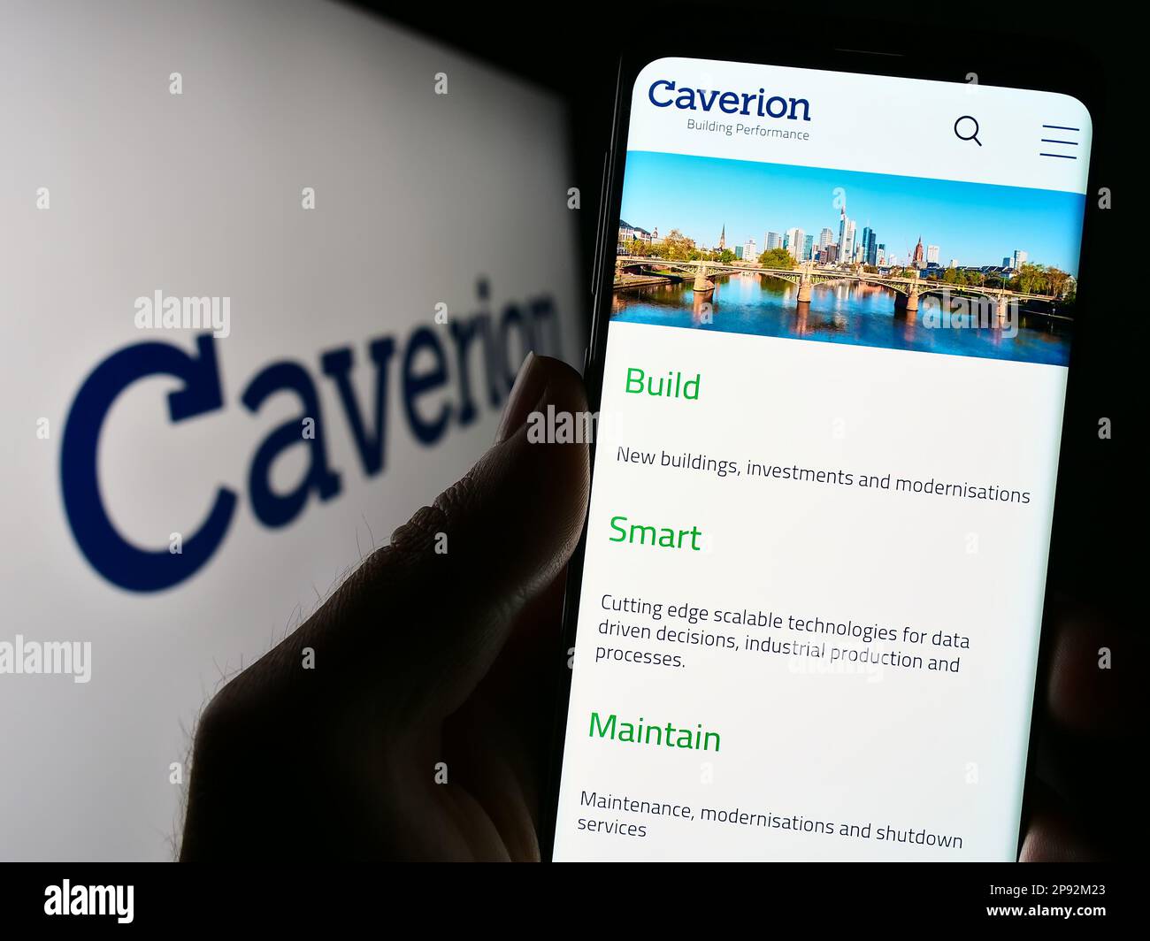 Person holding cellphone with website of building technology company Caverion Oyj on screen in front of logo. Focus on center of phone display. Stock Photo