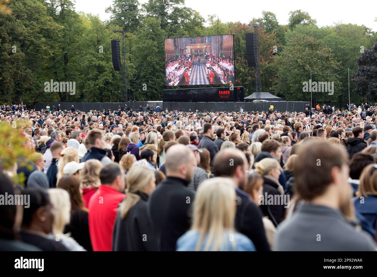 People watch the TV coverage of the late Queen Elizabeth II’s funeral day on a large screen in Hyde Park, London. Stock Photo
