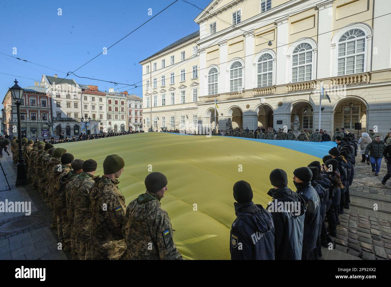 Lviv, Ukraine. 10th Mar, 2023. Military personnel, cadets and policemen sing the national anthem while holding a huge Ukrainian flag in front of the city hall Ratusha in honor of the anniversary of the first performance of the national anthem 158 years ago. (Photo by Mykola Tys/SOPA Images/Sipa USA) Credit: Sipa USA/Alamy Live News Stock Photo