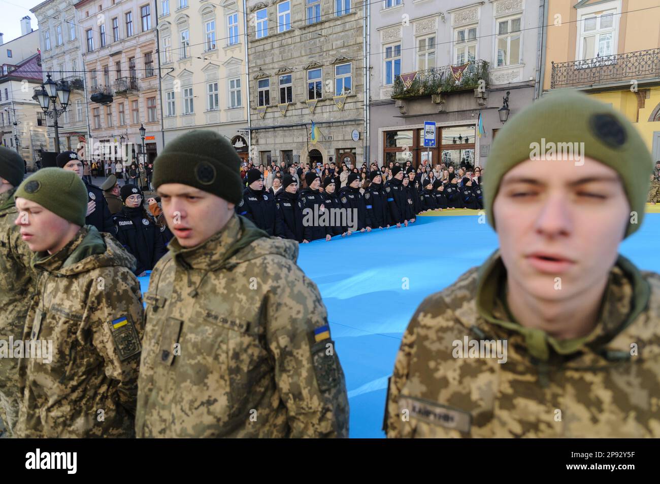 Lviv, Ukraine. 10th Mar, 2023. Military personnel, cadets and policemen sing the national anthem while holding a huge Ukrainian flag in front of the city hall Ratusha in honor of the anniversary of the first performance of the national anthem 158 years ago. (Photo by Mykola Tys/SOPA Images/Sipa USA) Credit: Sipa USA/Alamy Live News Stock Photo