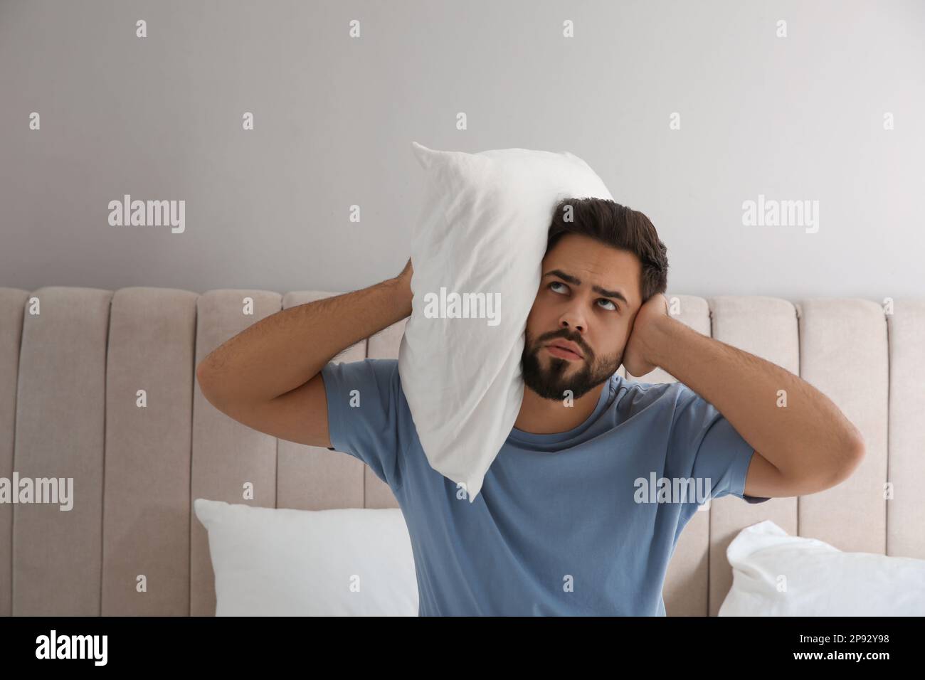 Unhappy young man covering ears in bed at home. Noisy neighbours Stock Photo