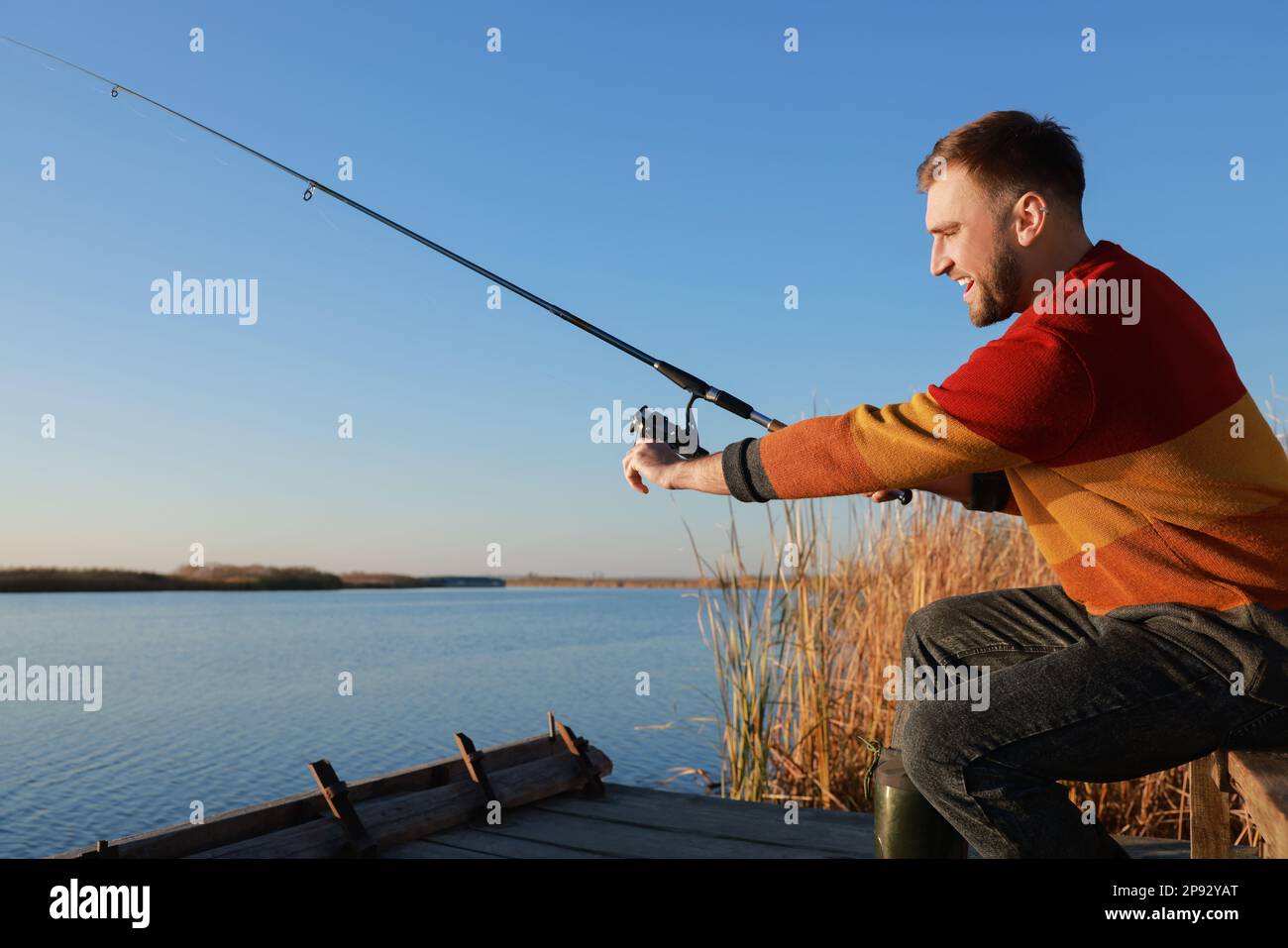Fisherman with fishing rod at riverside on sunny day Stock Photo