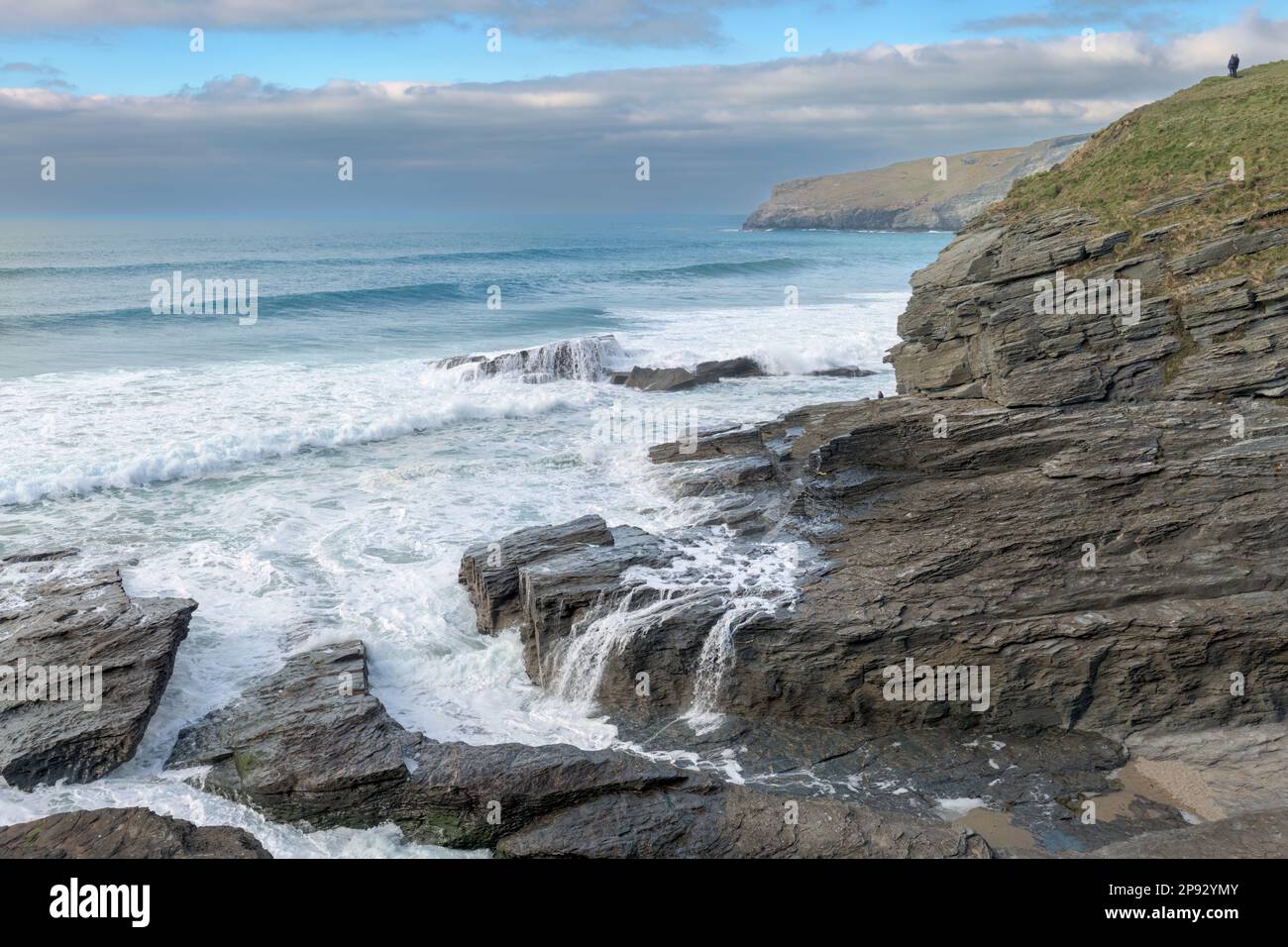 A couple watch the incoming tide from the top of the cliffs at Trebarwith Strand on the north coast of Cornwall, England. Stock Photo