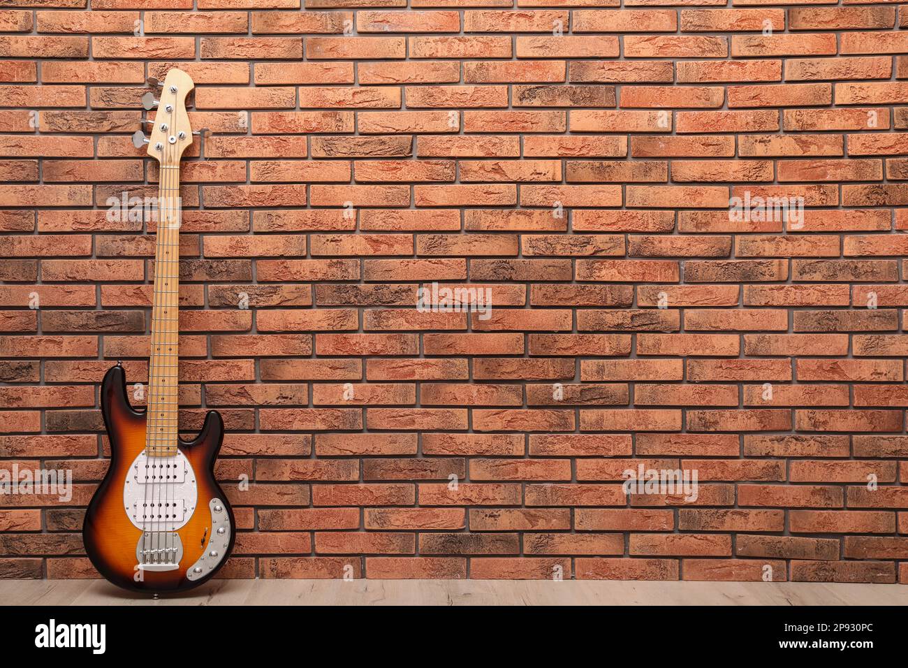 Modern electric guitar near red brick wall indoors. Space for text Stock Photo Alamy
