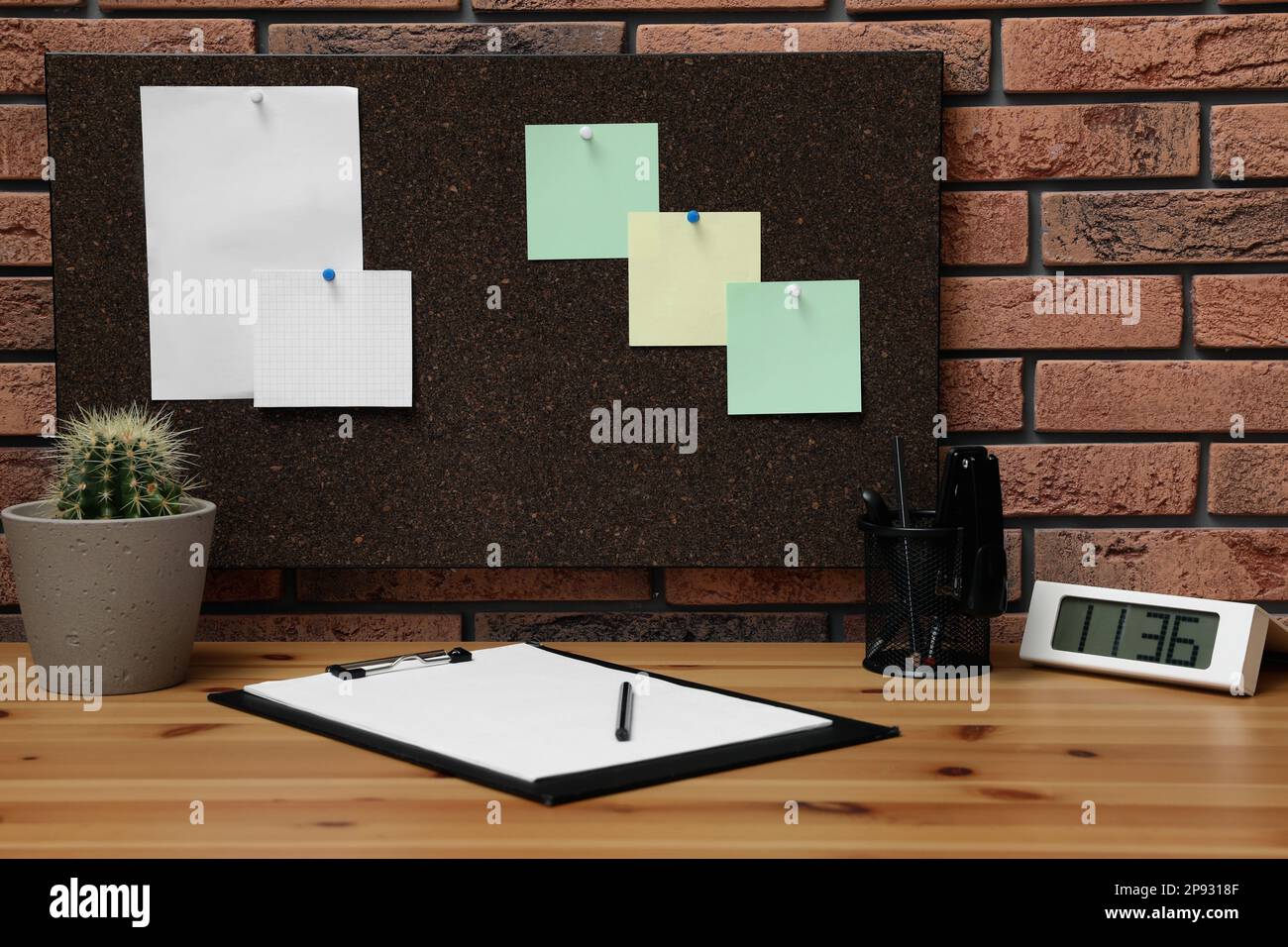Corkboard with pinned notes hanging on brick wall over desk in office