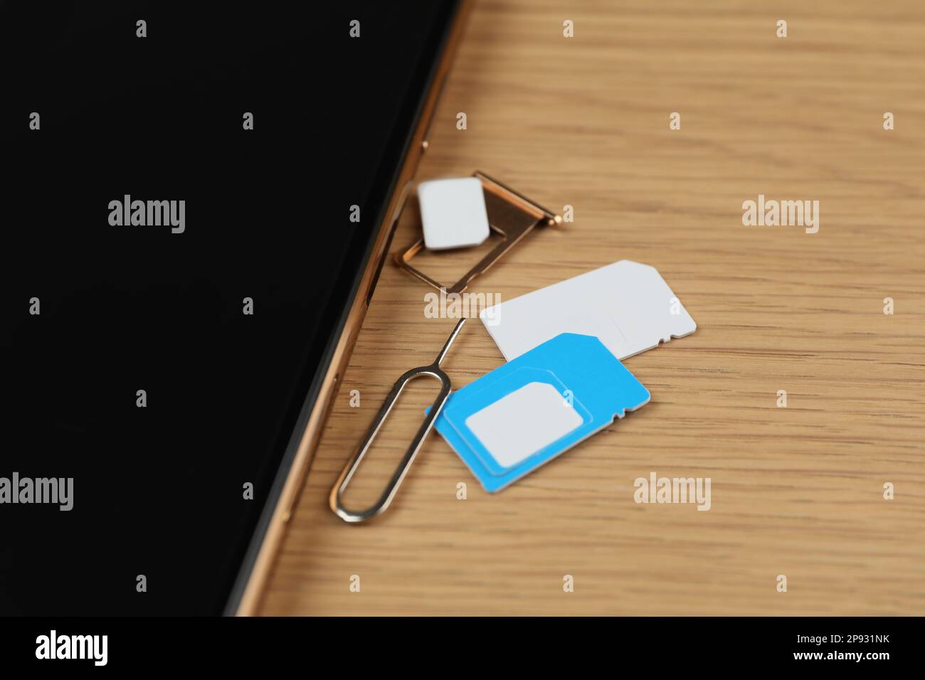 SIM cards, mobile phone and ejector tool on wooden table, closeup Stock Photo