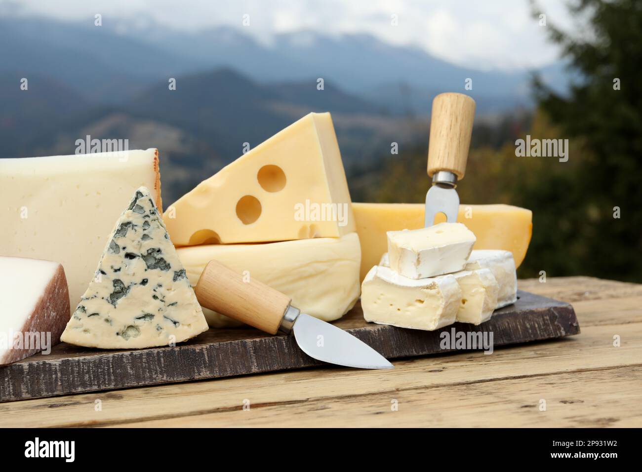 Different types of delicious cheeses on wooden table against mountain ...