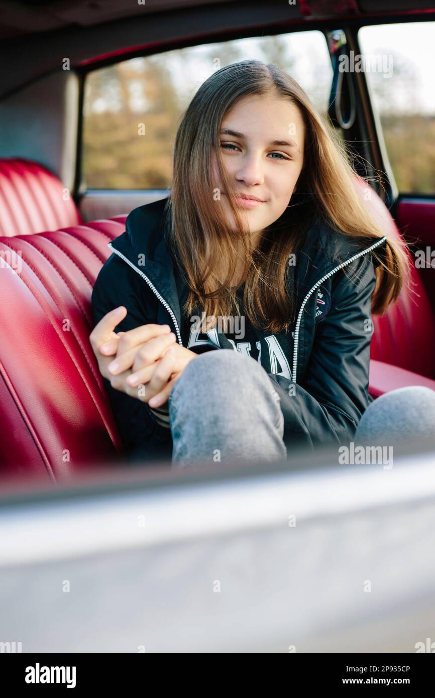Girl sitting smiling in old car with red leather seats looking at camera Stock Photo