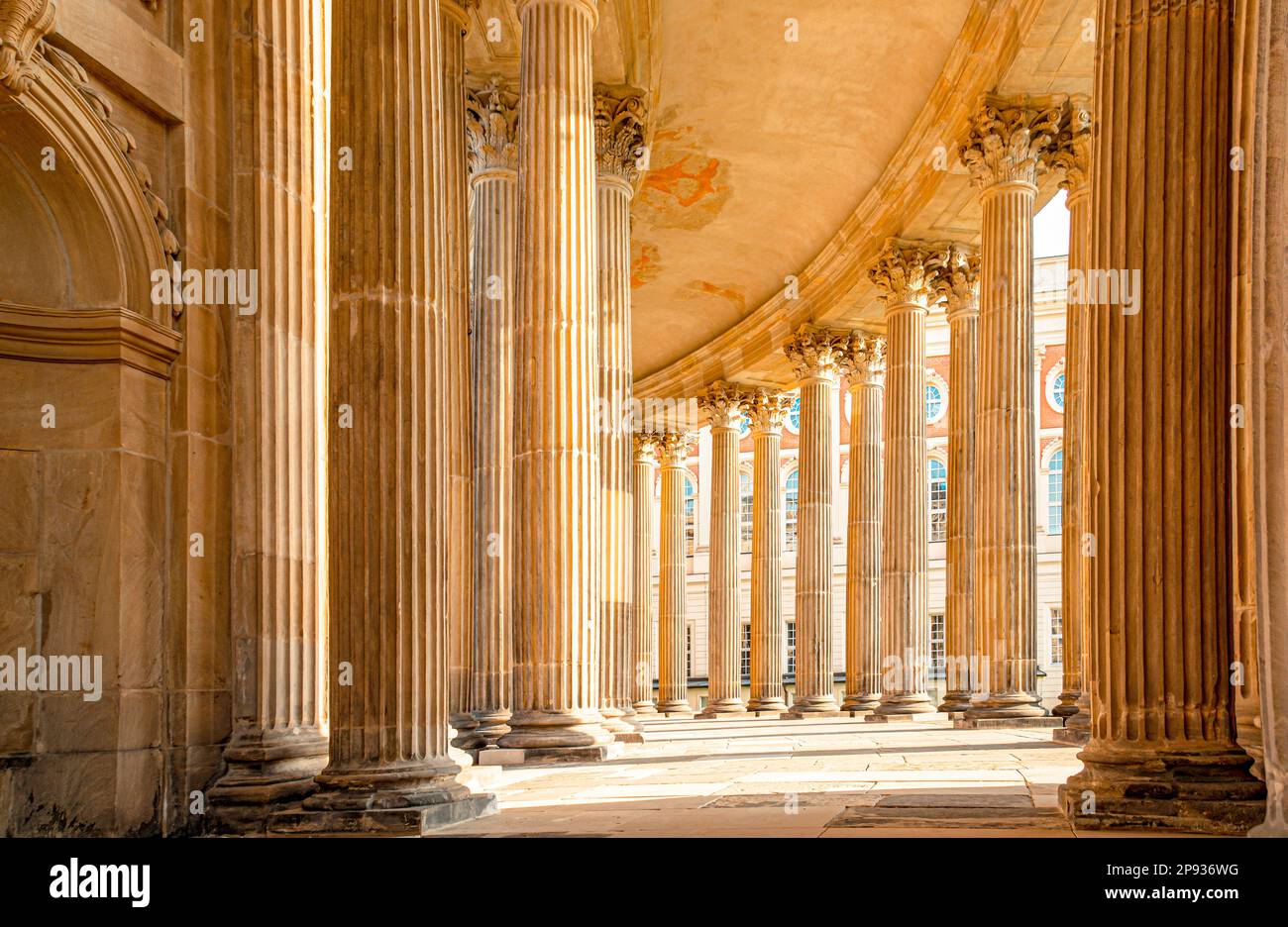 View into the ring-shaped colannades of the Neues Palais in Potsdam with symmetrical columns and Neues Palais in the background Stock Photo
