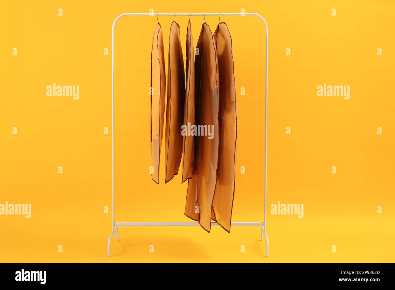 Garment bags with clothes on rack against yellow background Stock Photo