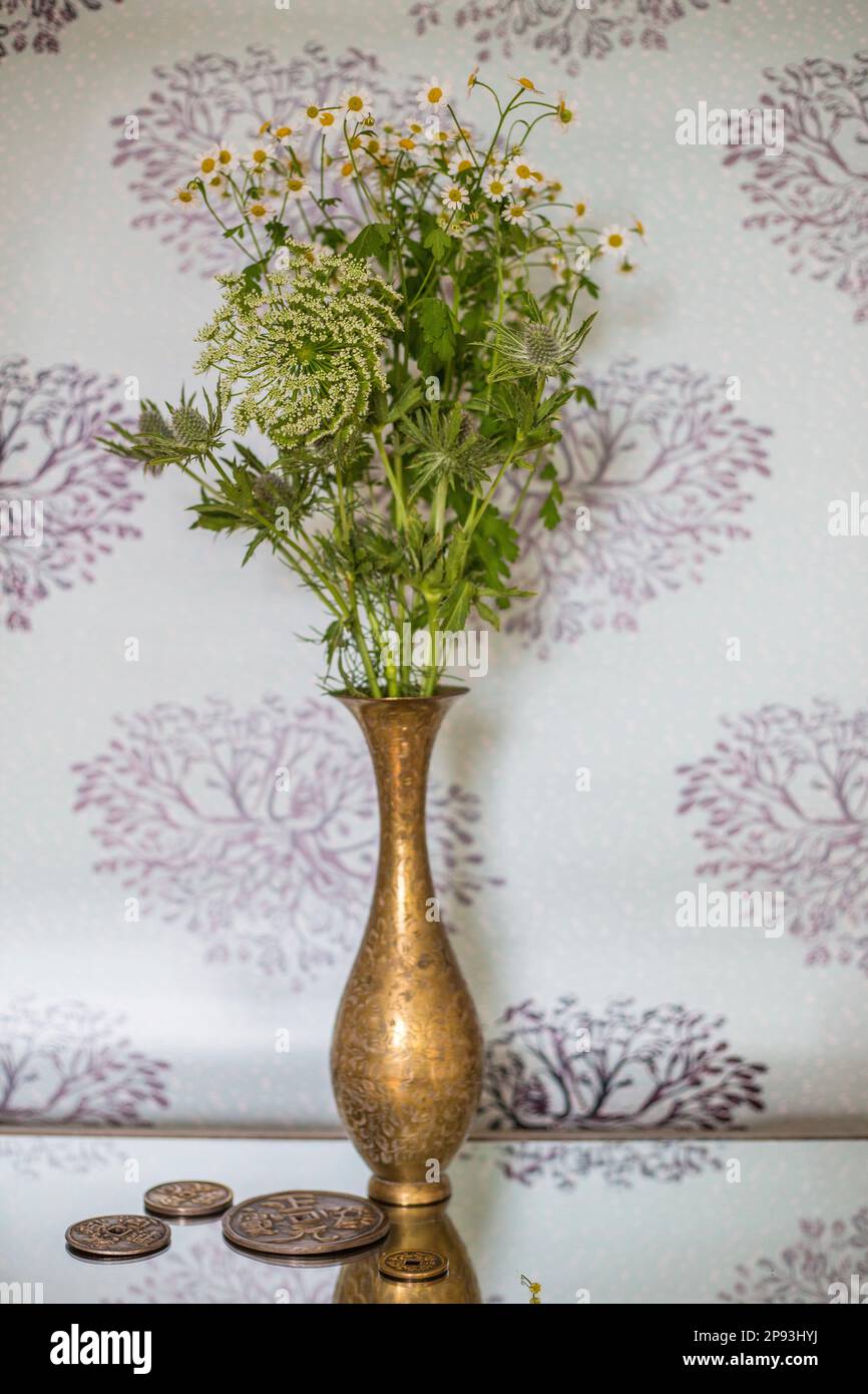 Golden flower vase with a bouquet of meadow flowers on a mirrored table Stock Photo