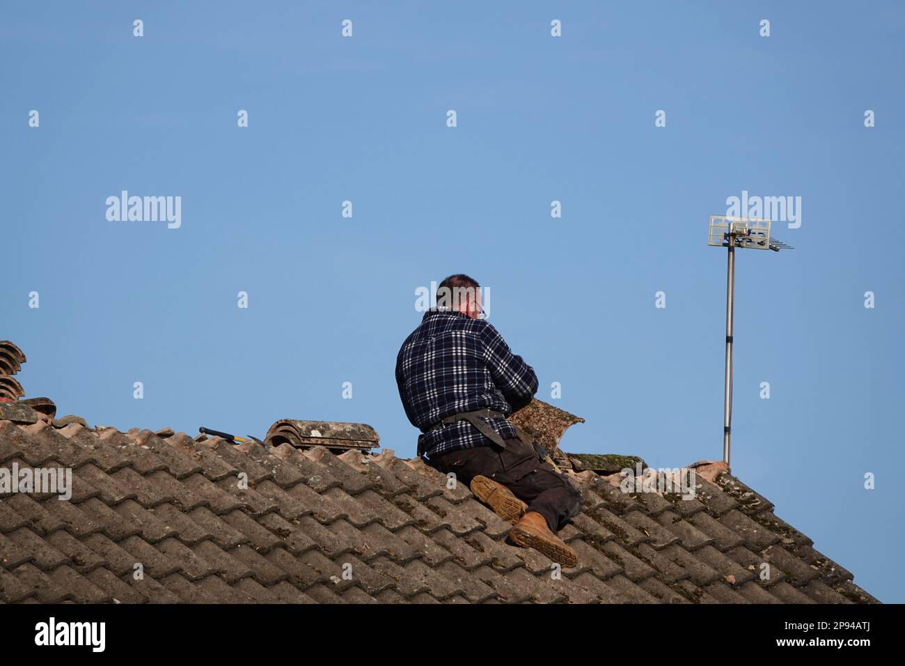 A roofer repairing ridge tiles on the roof of a domestic house Stock Photo