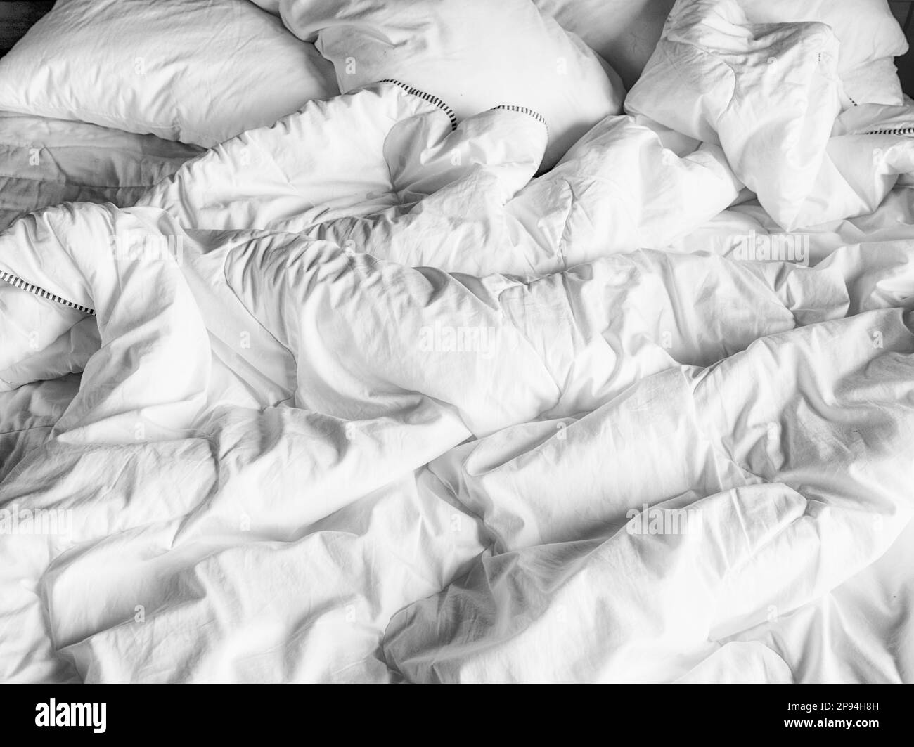 Domestic background of the rumpled duvet cover, white sheets and pillows on a bed. Stock Photo