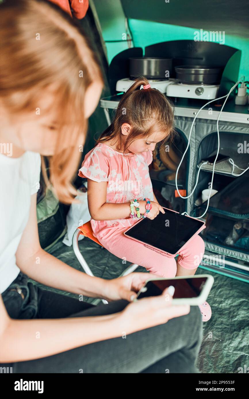 Sisters spending family time in a tent on camping. Children using tablet playing games online during summer vacation Stock Photo