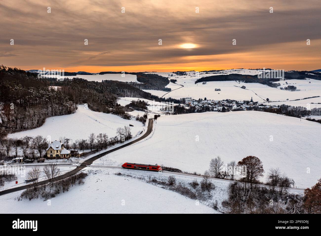 Germany, Thuringia, Bechstedt, Allendorf (background), regional train 60, train 29886, stop, house (former reception building), landscape, village, fields, forests, snow, overview, sunset shimmers through the clouds, back light Stock Photo