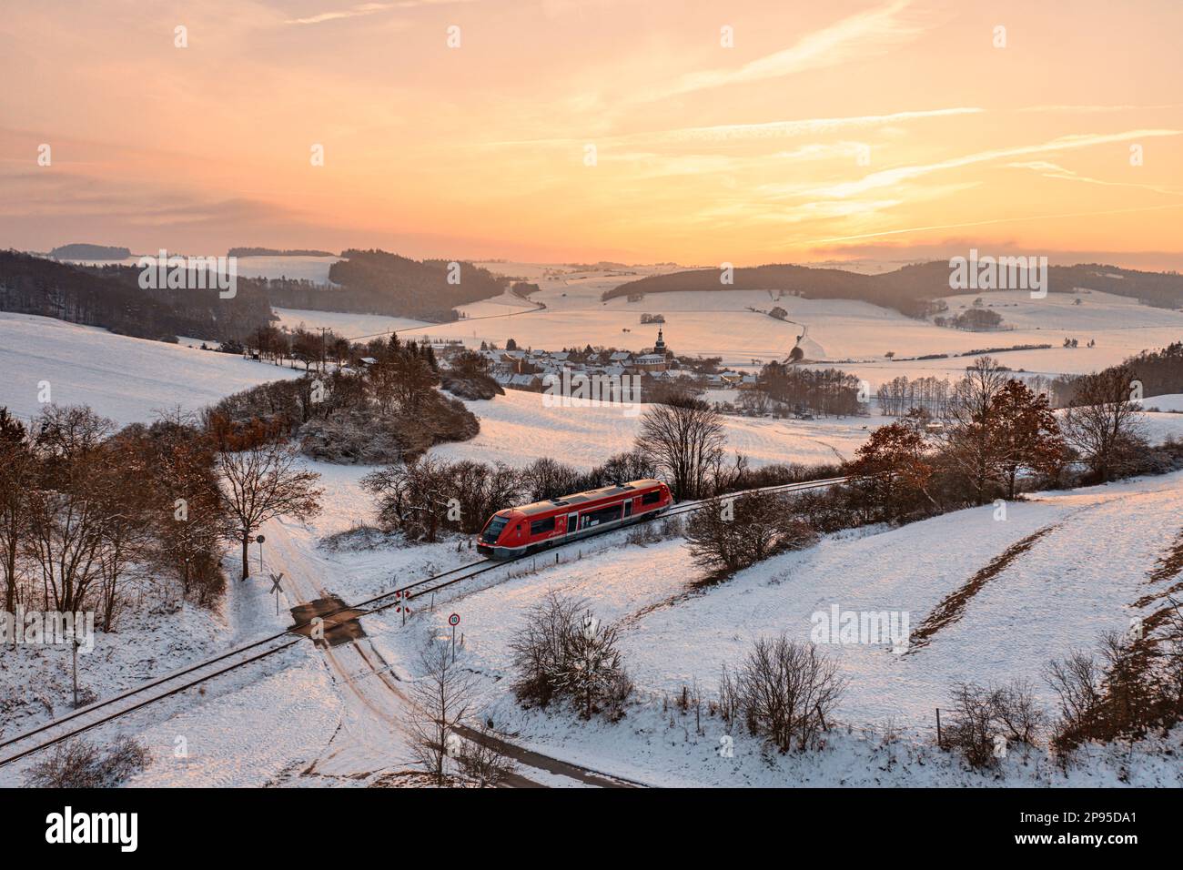 Germany, Thuringia, Allendorf, regional train 60, train 29889, level crossing, landscape, village, fields, forests, snow, overview, evening light, back light Stock Photo