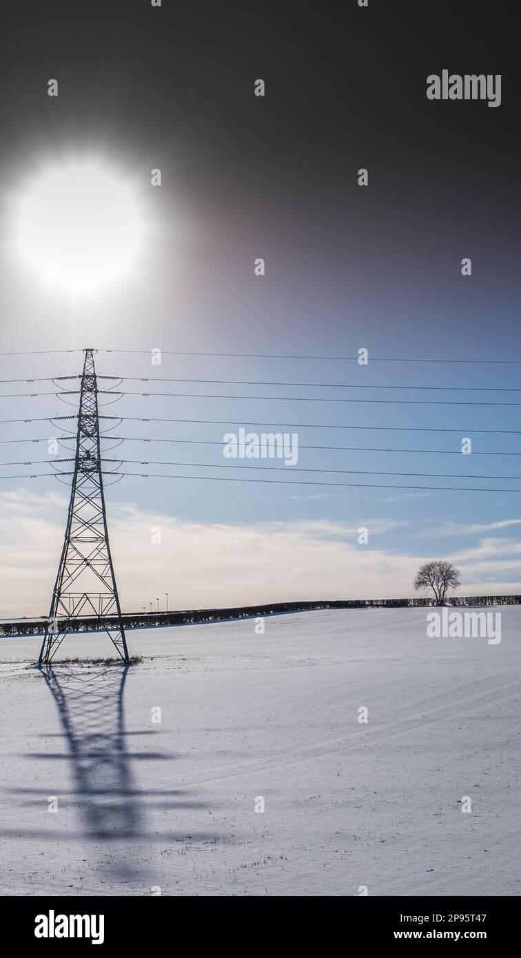 High voltage overhead cables transmission lines operating at 275kV with glass insulators crossing a snow covered field with shadow and sun. Stock Photo