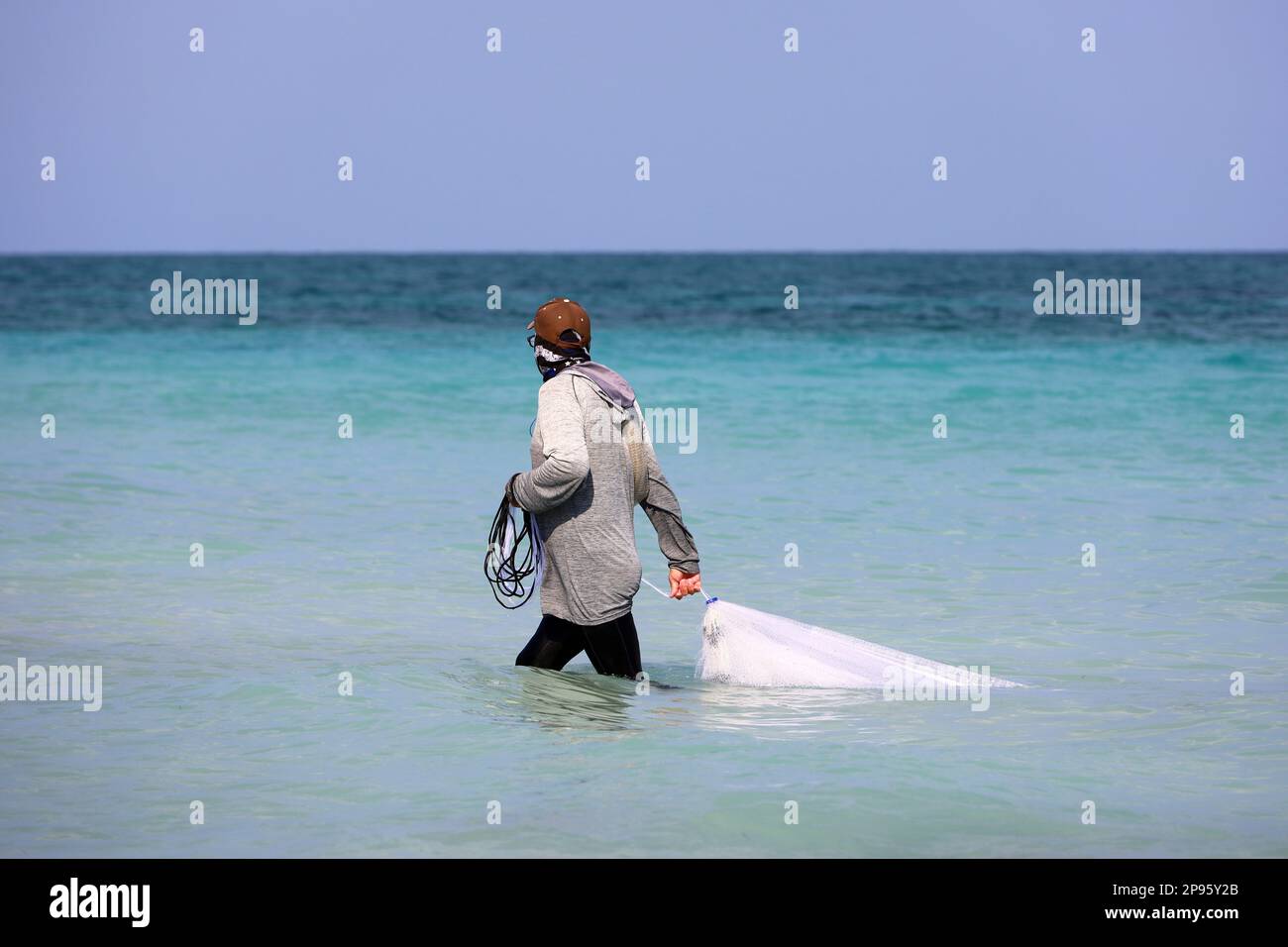 Fisherman with fishing net goes in water by the sea shore. Traditional fishing on Caribbean islands Stock Photo