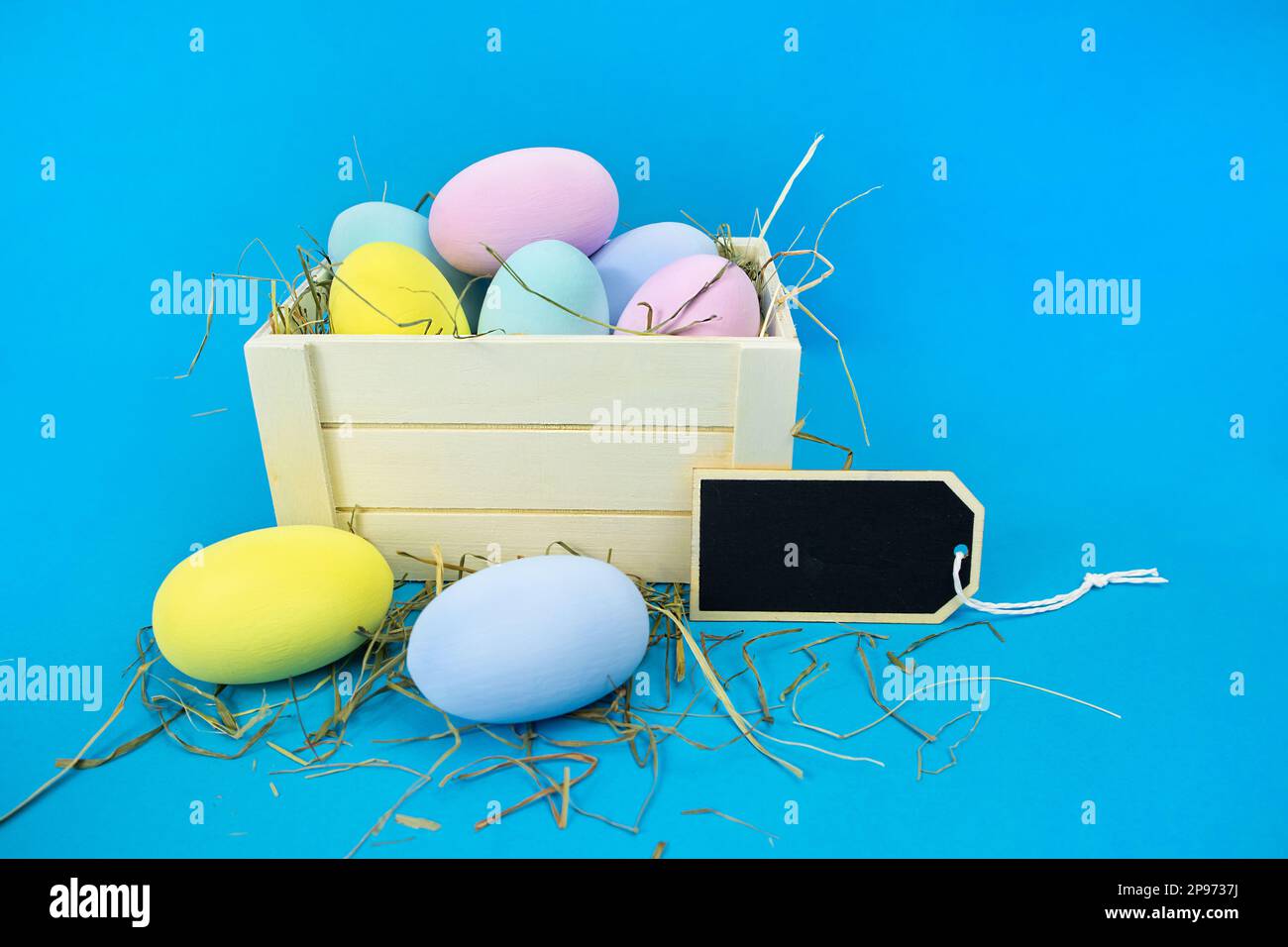 Easter moc-up. Wooden box with straw and colorful eggs on a blue background. Stock Photo