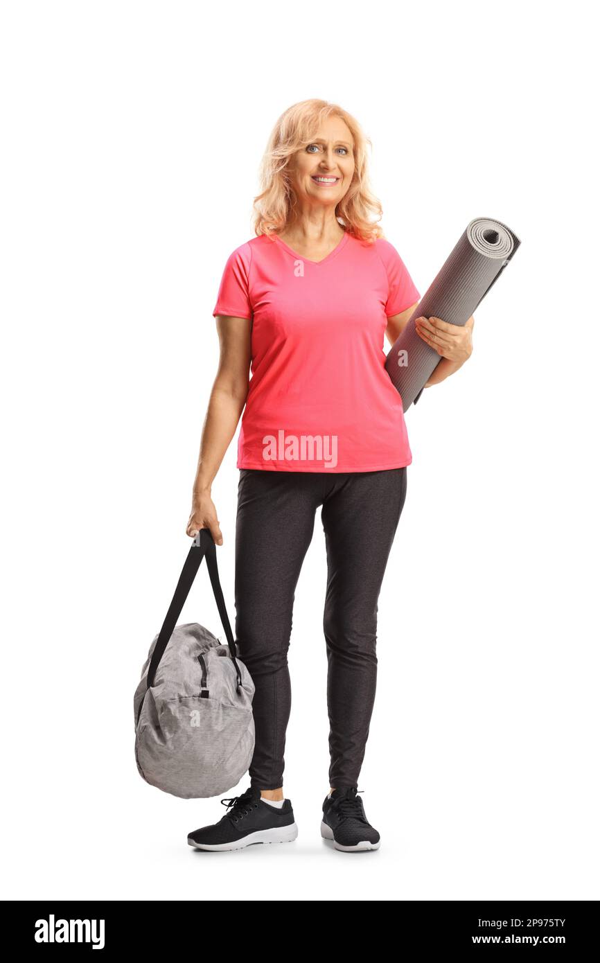 Full length portrait of a mature woman in sport clothes holding an exercise mat and a sports bag isolated on white background Stock Photo
