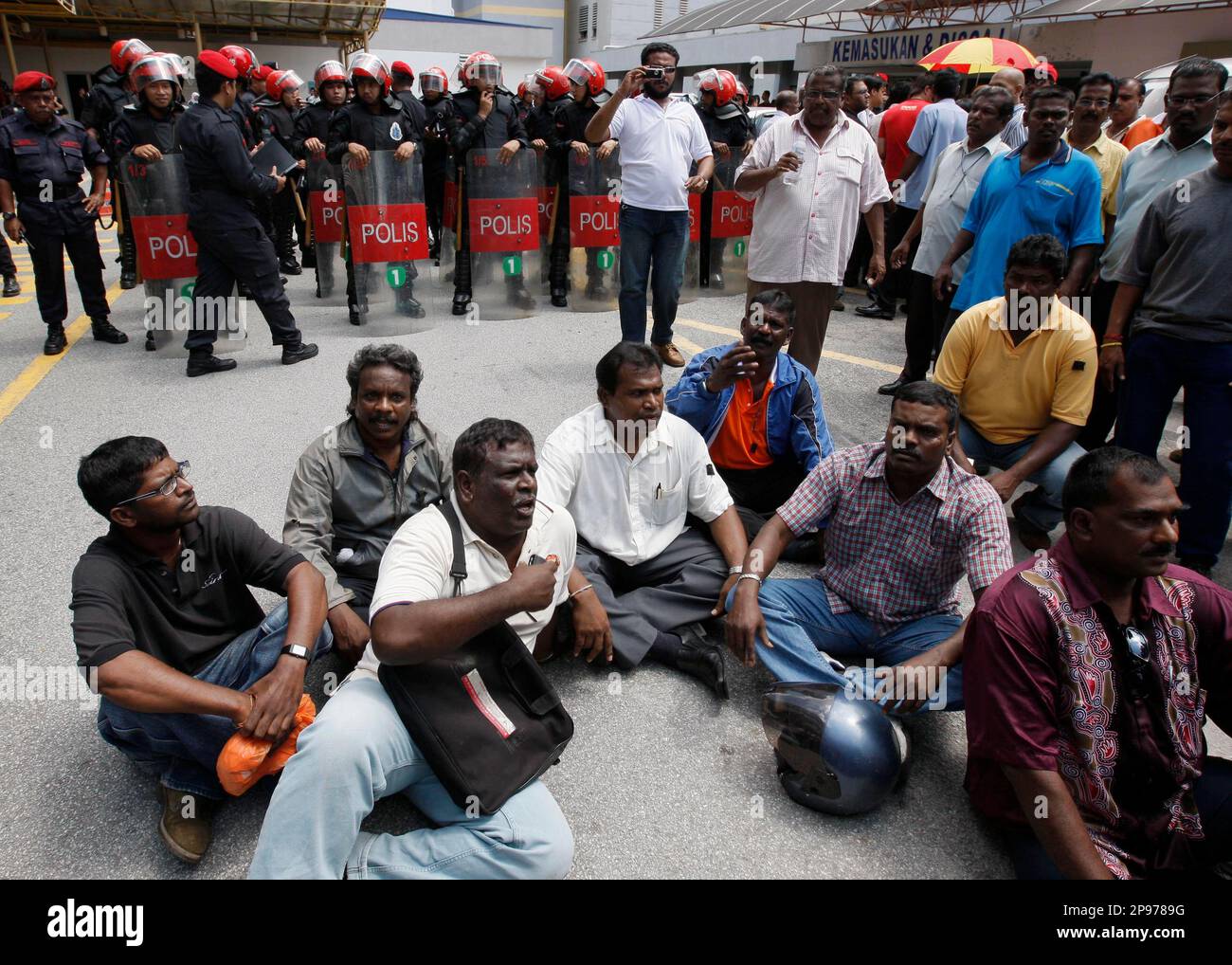 Family members and friends of Ananthan Kugan sit outside the forensic department at the University of Malaya Medical Center as riot police look on in Kuala Lumpur, Malaysia, Wednesday, Jan. 28, 2009. Hundreds of ethnic Indians gathered amid tight security near Malaysia's largest city Wednesday to mourn 22-year-old Kugan whose family believes he was killed by police while in custody. Activists say more than 80 detainees - mainly from the ethnic Indian minority - have died under questionable circumstances in the past decade. (AP Photo/Vincent Thian) Stock Photo