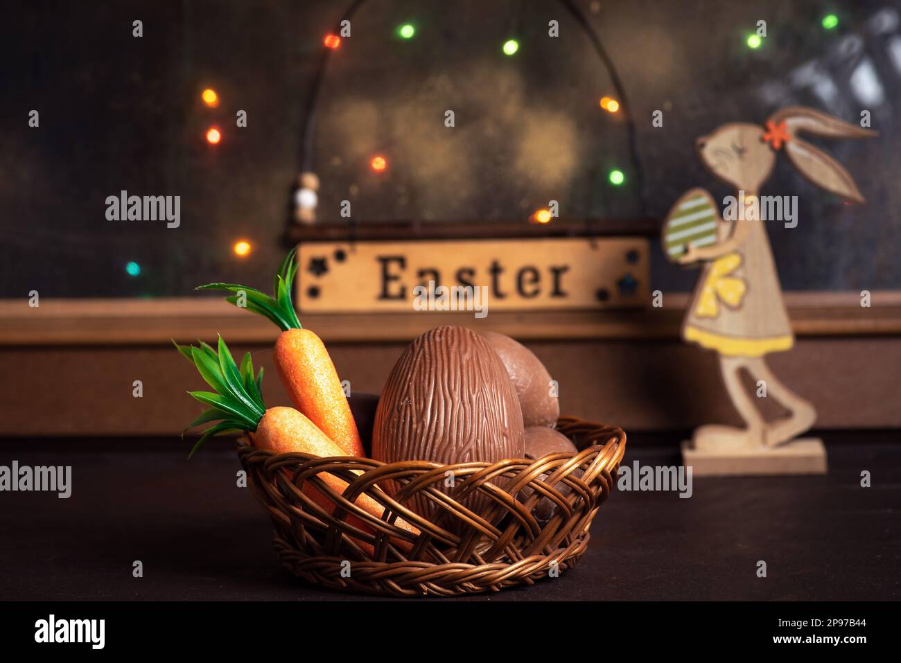 Easter decoration. A wooden bunny with colorful Easter eggs in front of the window on a wooden table. Stock Photo