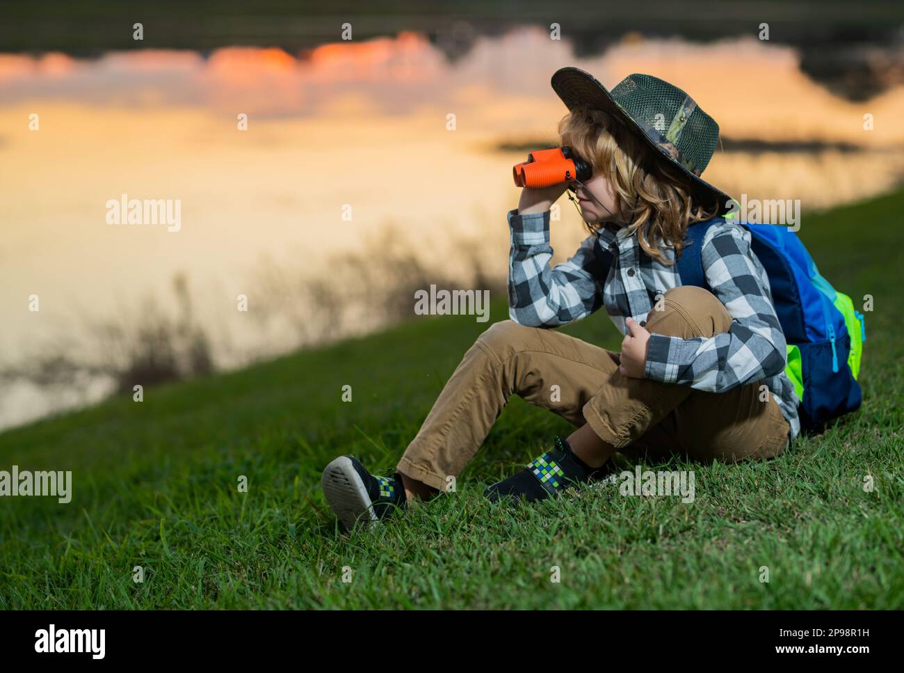 Young boy looking through binoculars. Little explorer. Outdoor recreation and adventures with kids. Child tourist on sunny countryside background Stock Photo