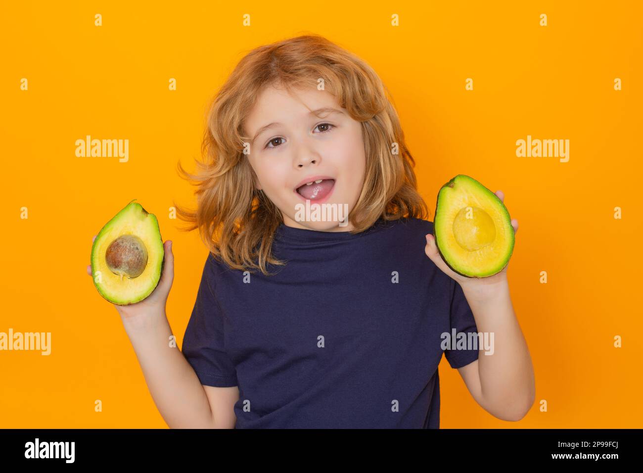 Kid hold red avocado in studio. Studio portrait of cute child with avocado isolated on yellow background, copy space Stock Photo