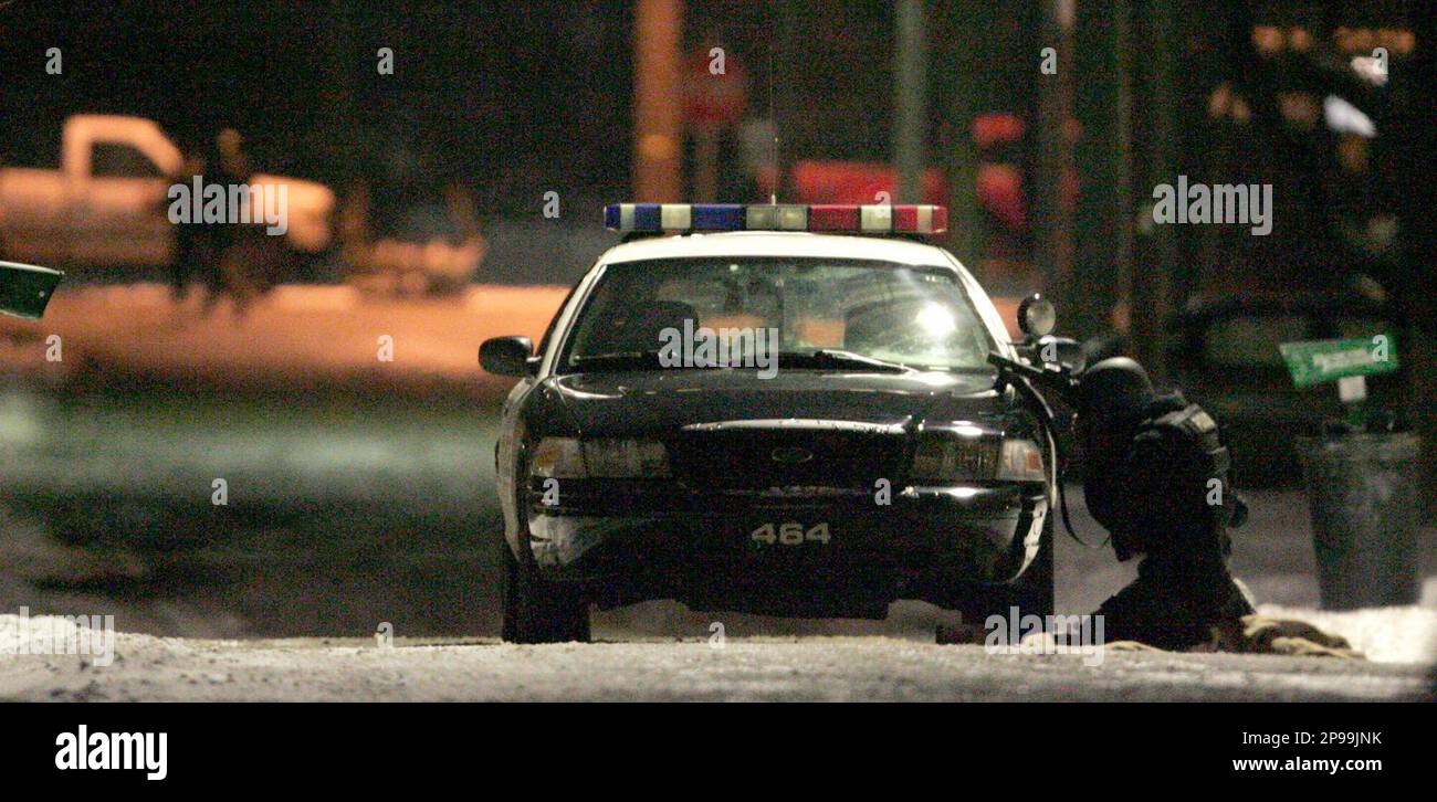 A Metro SWAT officer takes cover behind a police car in front of a home