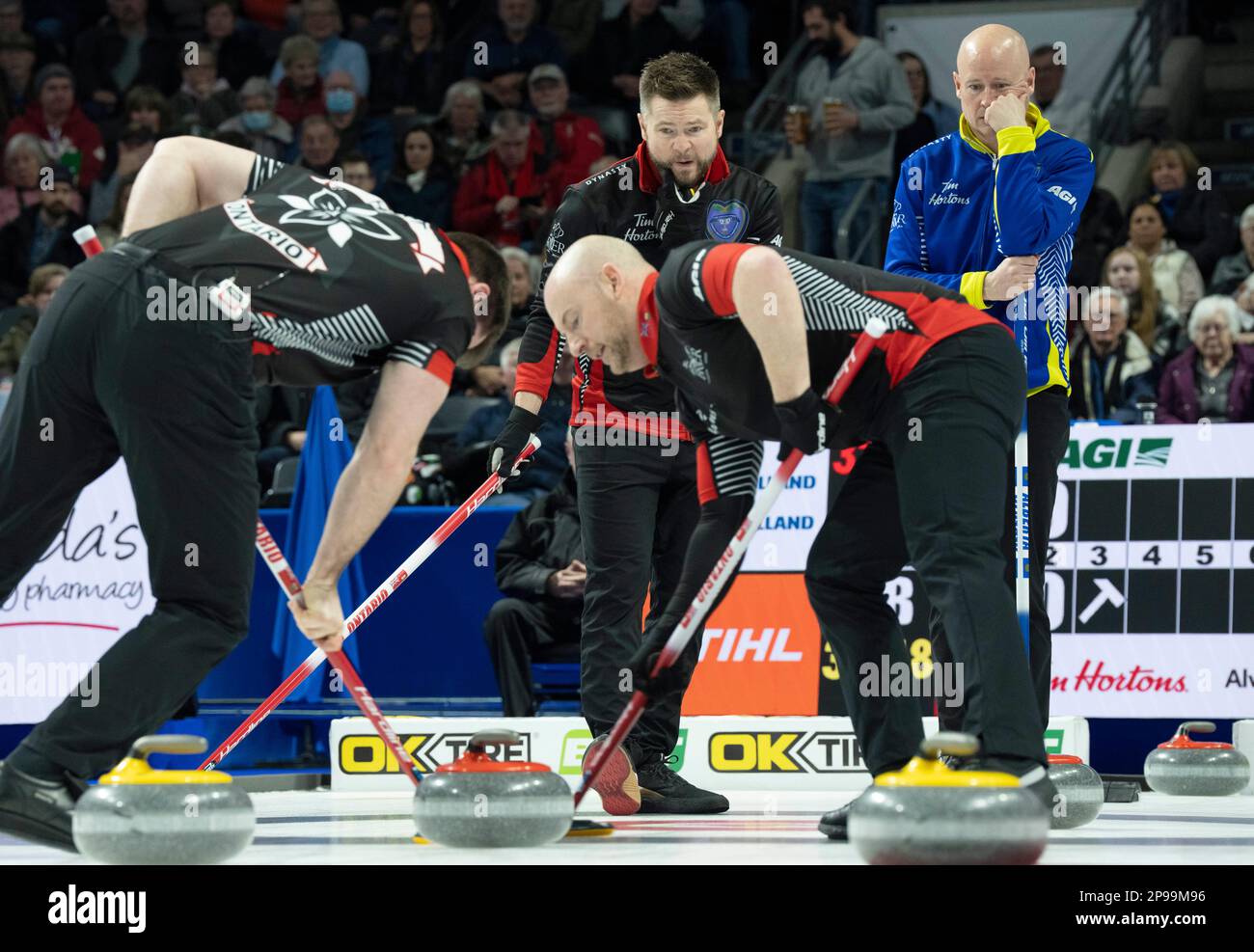March 10, 2023, London, ON, Canada Ontario skip Mike McEwan (left back) and Alberta skip Kevin Koe (right back) watch as Ontario lead Joey Hart (left) and third Ryan Fry (right) sweep