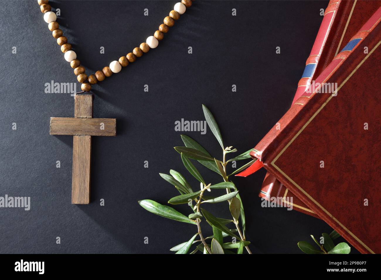 Easter religious background with symbols as books christian cross and olive branches on black table. Top view. Stock Photo