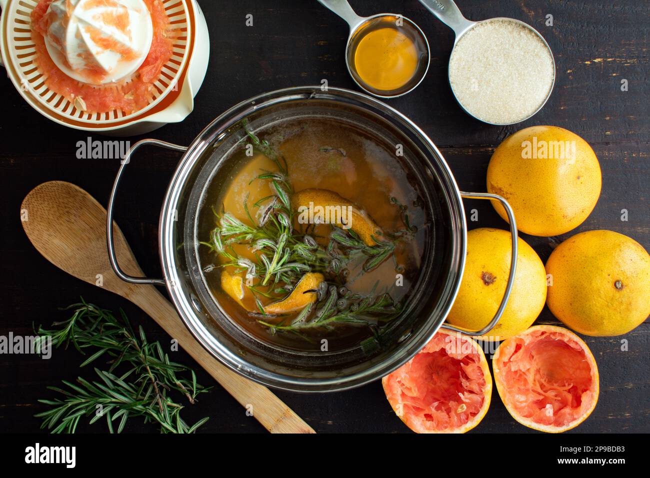 Making Rosemary-Grapefruit Simple Syrup in a Saucepan: Infused simple syrup surrounded by red grapefruit and other ingredients Stock Photo