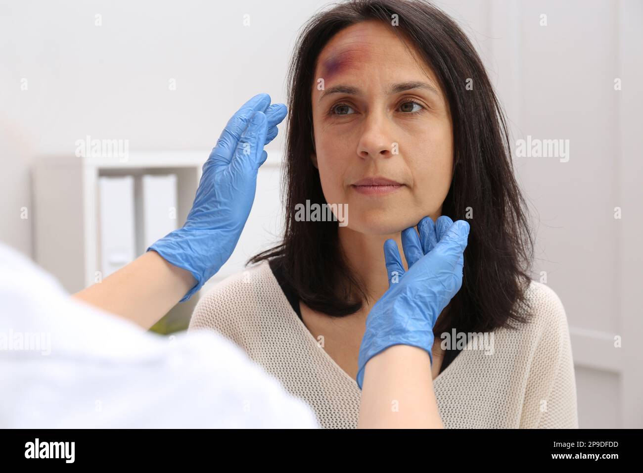 Doctor examining woman with bruise on forehead in clinic Stock Photo