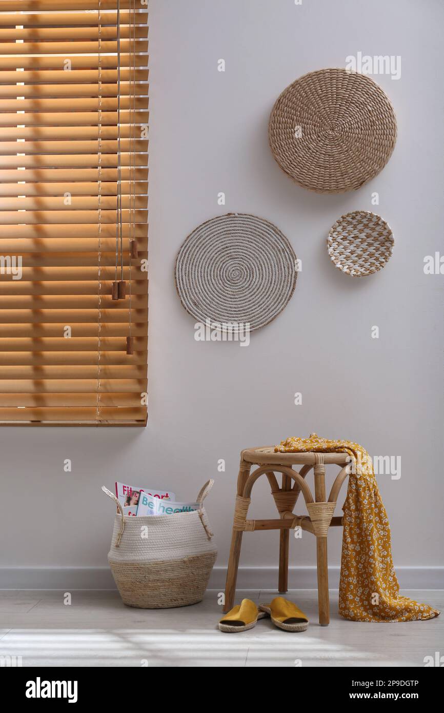 Wooden stool with dress and wicker basket near light  grey wall indoors. Interior accessories Stock Photo