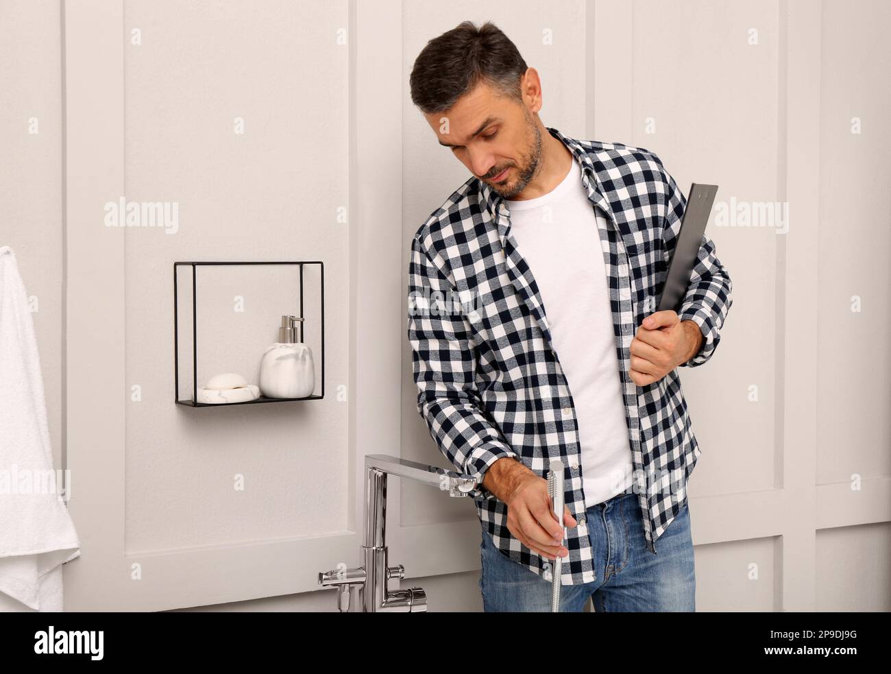 Plumber with clipboard checking water tap in bathroom Stock Photo