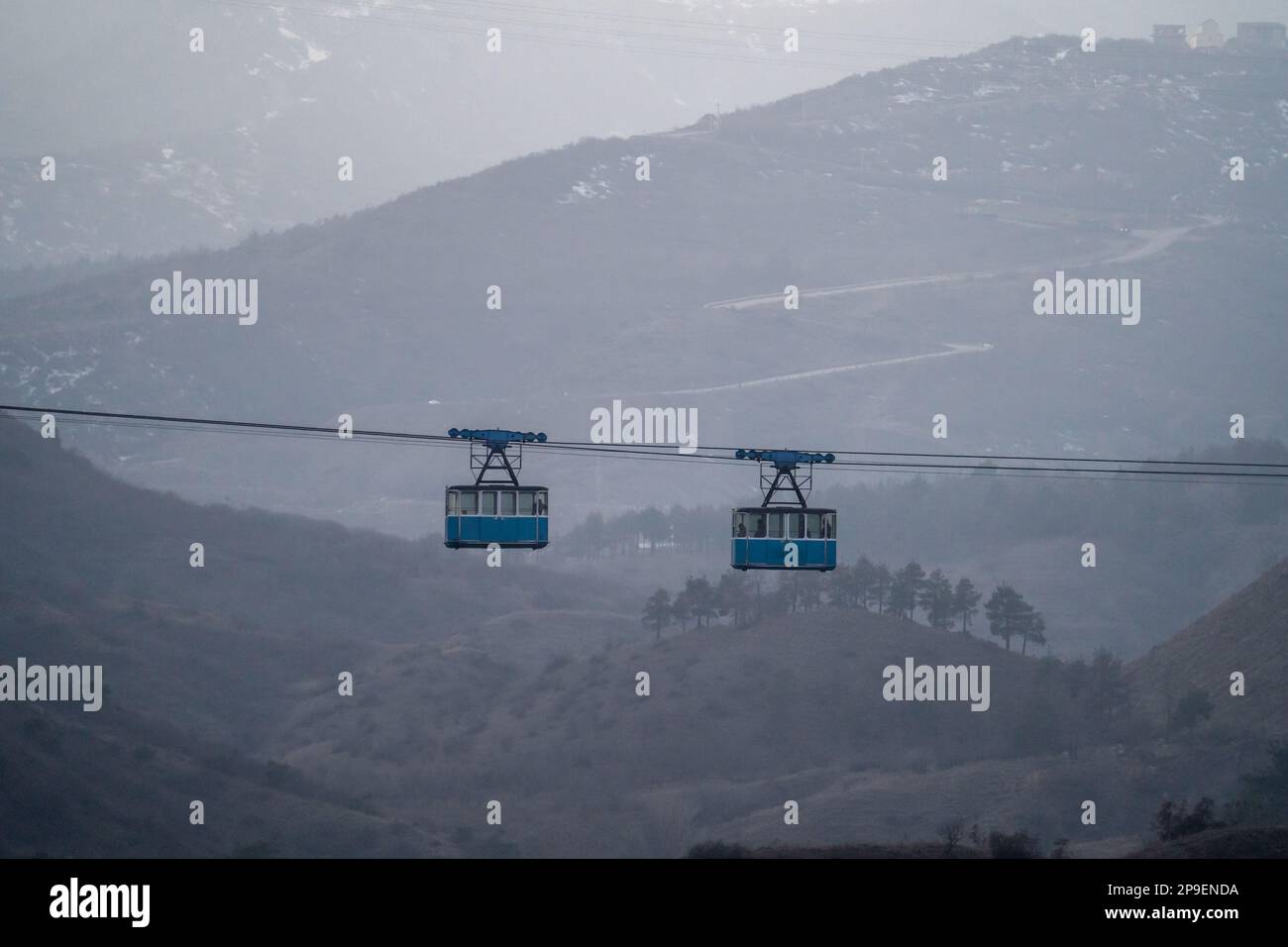 Two blue public old cabins of cable car moves against backdrop of misty ...