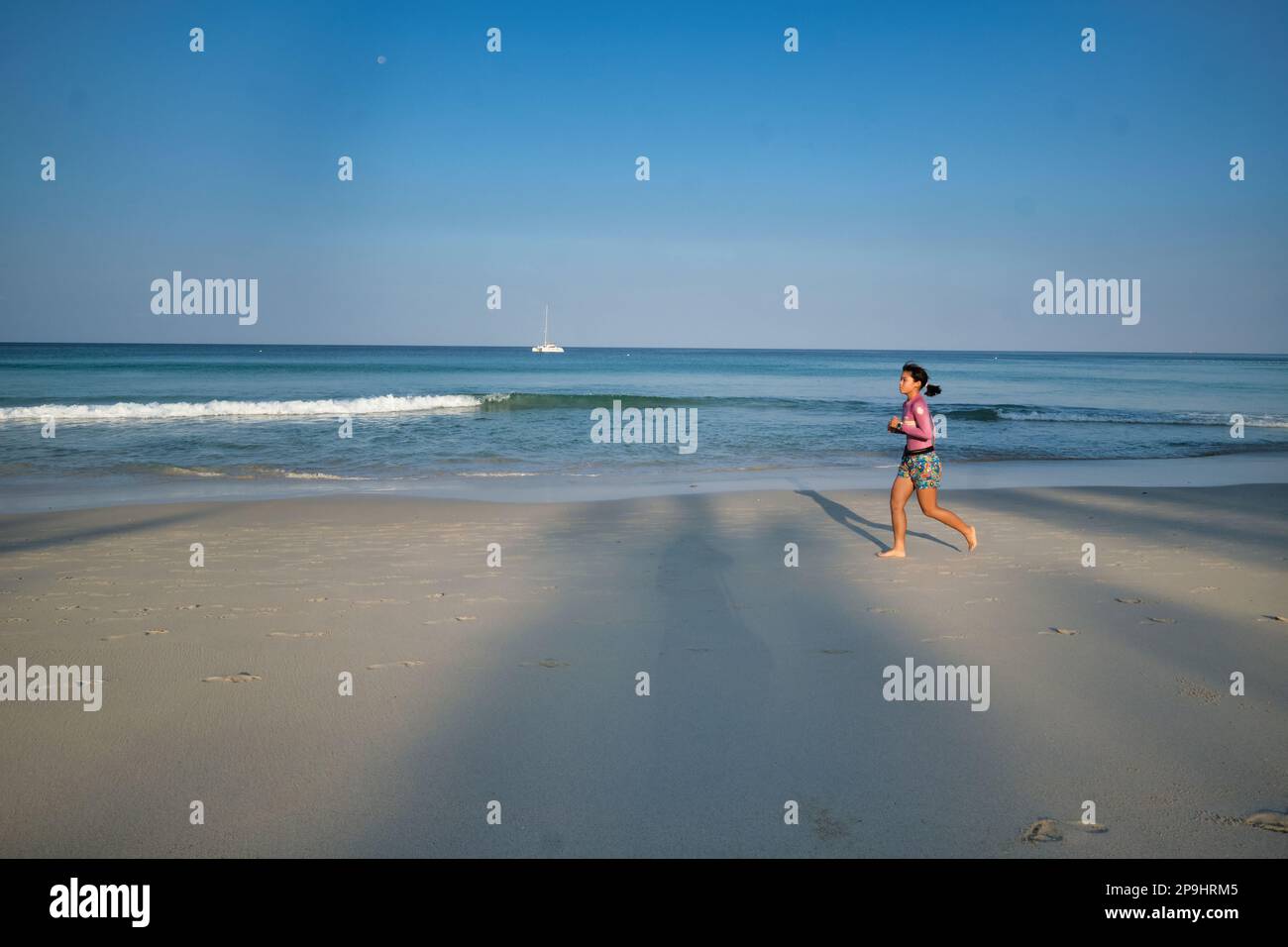 On an early morning, a lone female Asian woman is jogging along Kata Noi Beach, Phuket, Southern Thailand Stock Photo