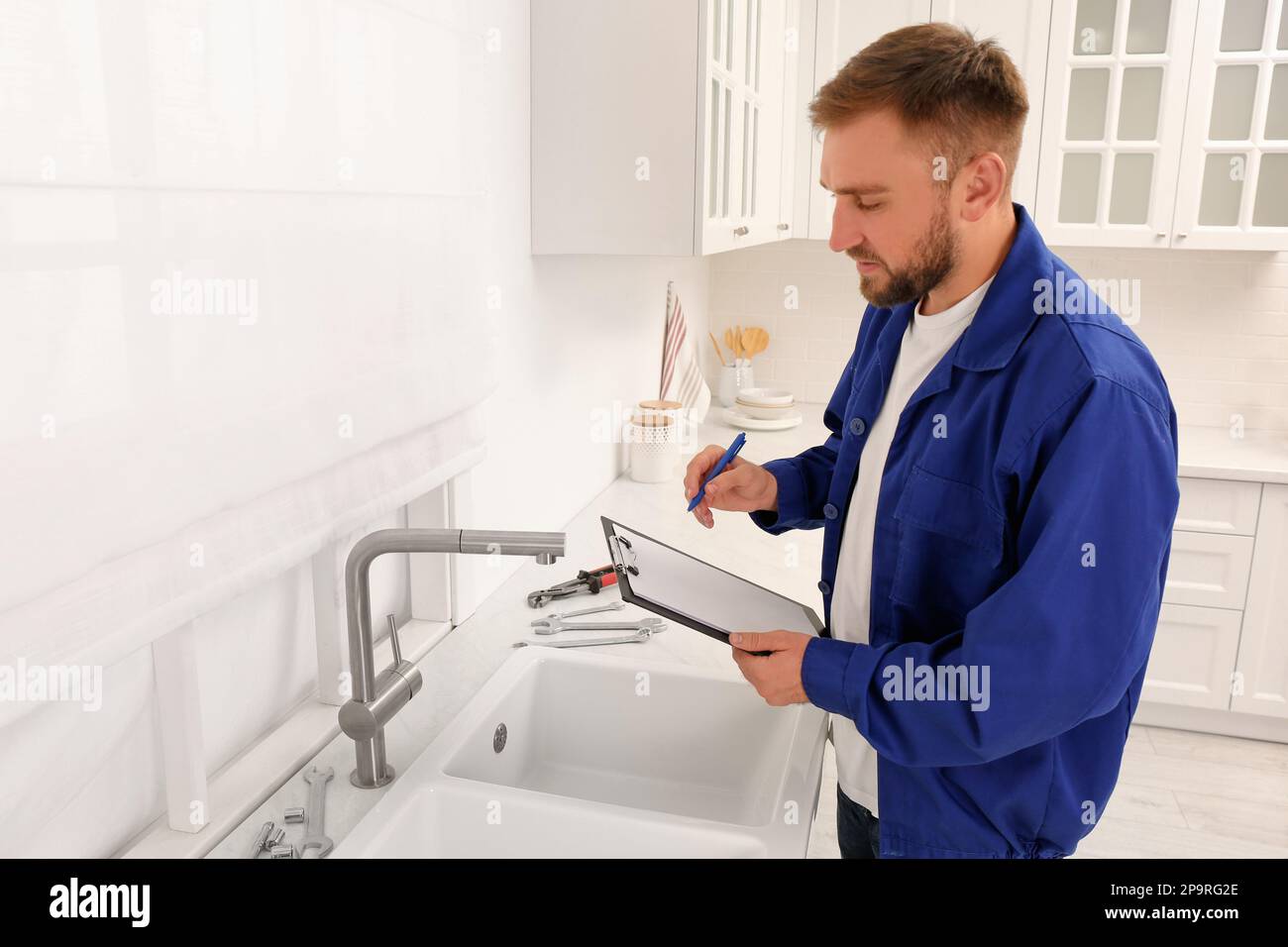Plumber with clipboard checking water tap in kitchen Stock Photo