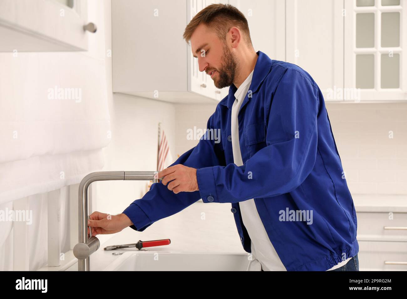 Plumber checking water tap after installation in kitchen Stock Photo