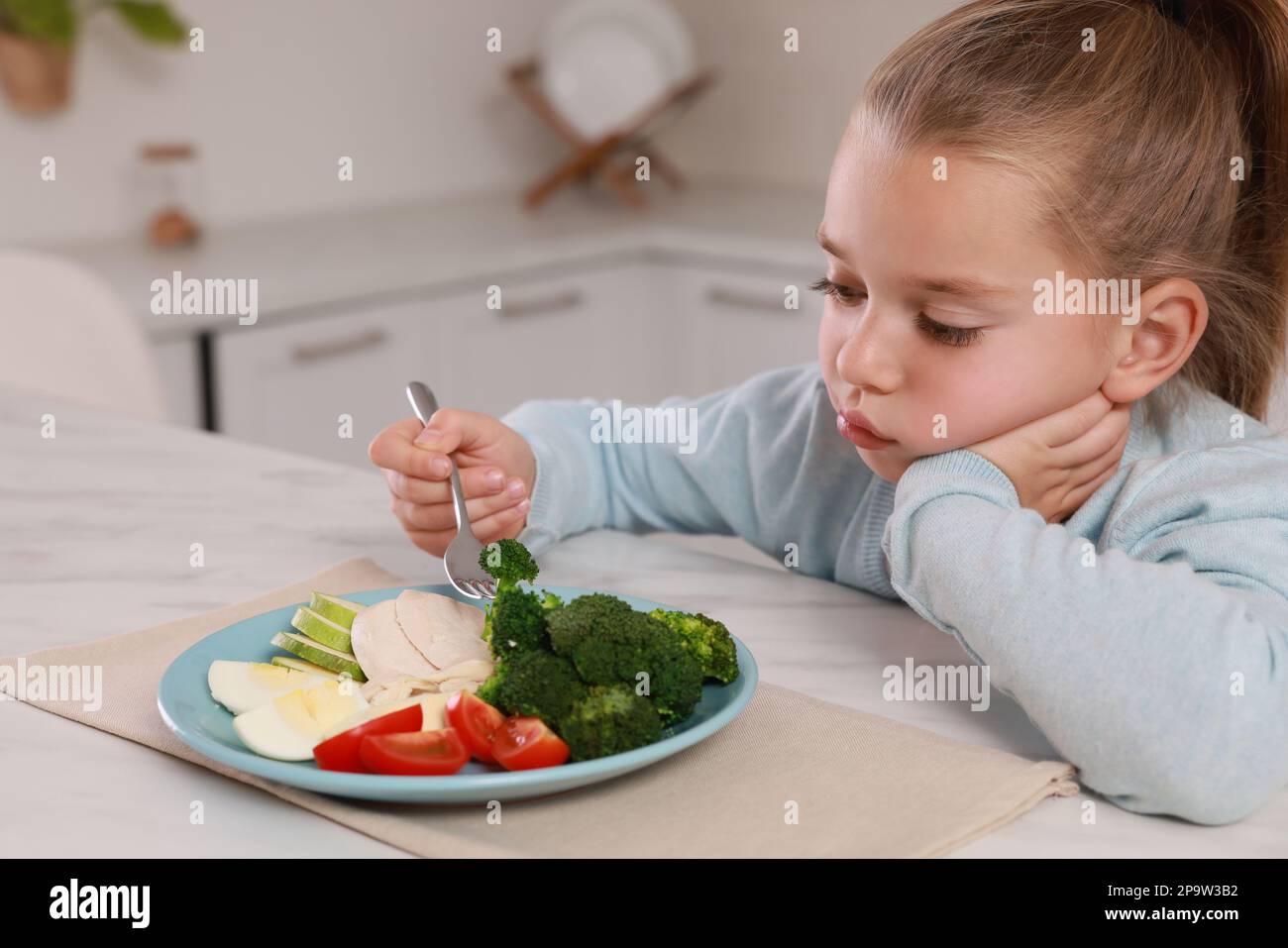 Cute little girl refusing to eat dinner in kitchen Stock Photo - Alamy