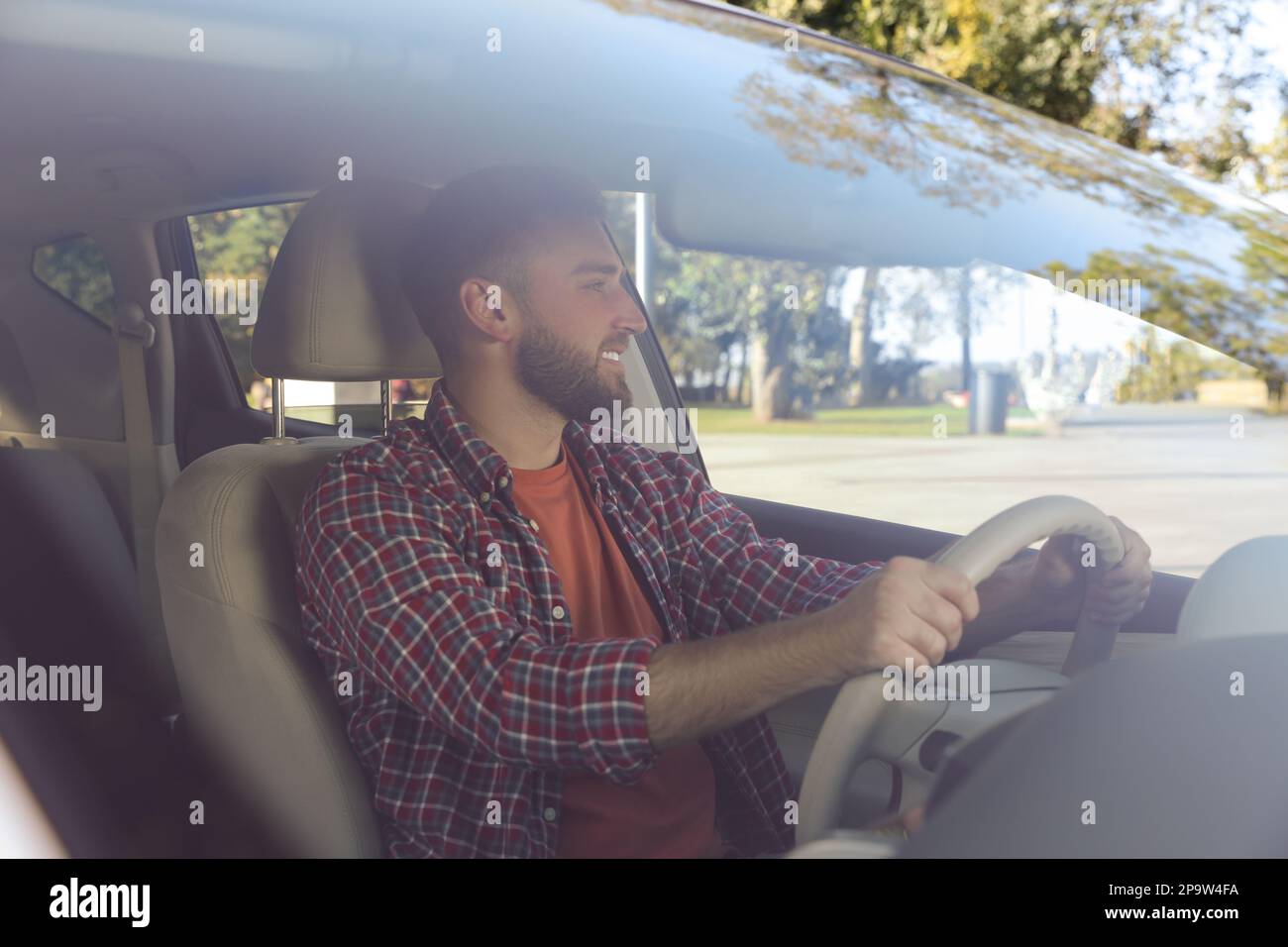 Handsome young driver sitting in modern car, view through windshield