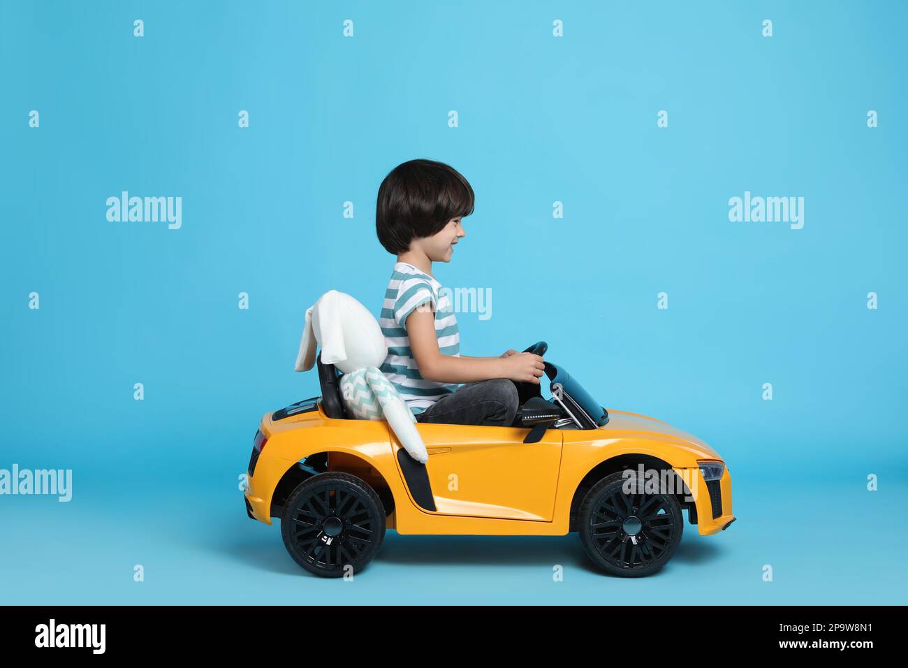 Cute little boy with toy bunny driving children's car on light blue background Stock Photo Alamy