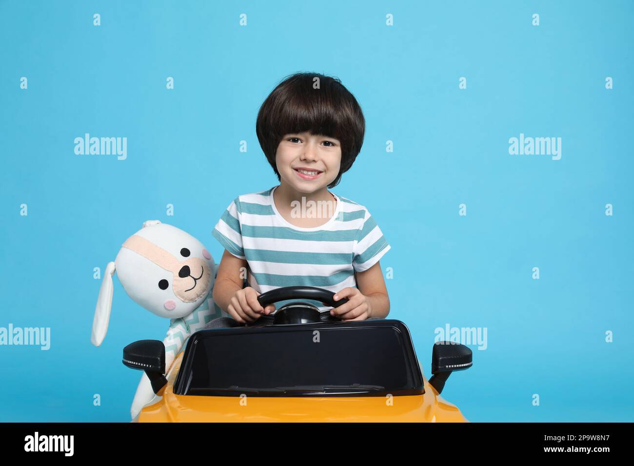Cute little boy with toy bunny driving children's car on light blue background Stock Photo Alamy