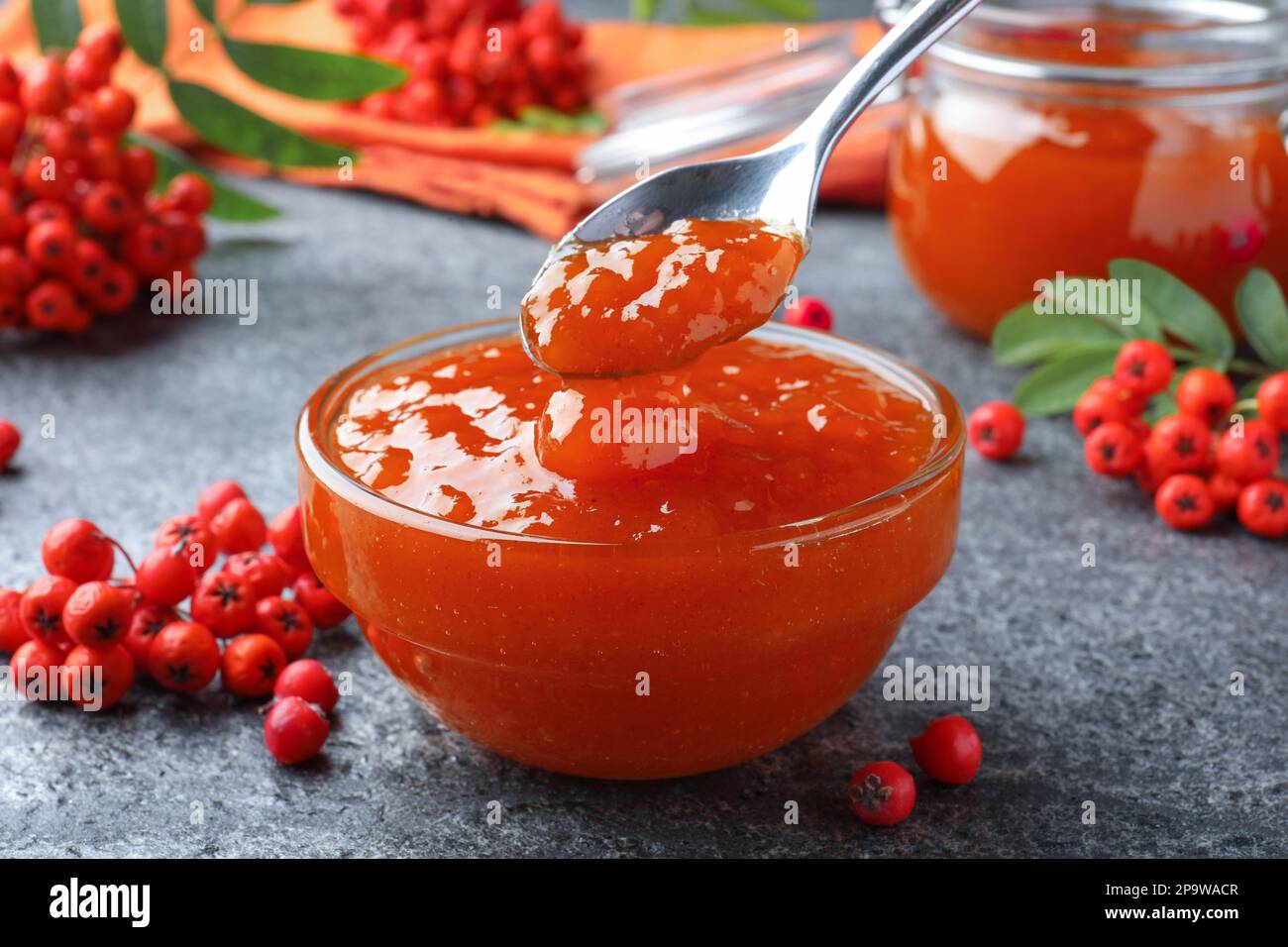 Delicious rowan jam in glass bowl and berries on grey table, closeup Stock Photo