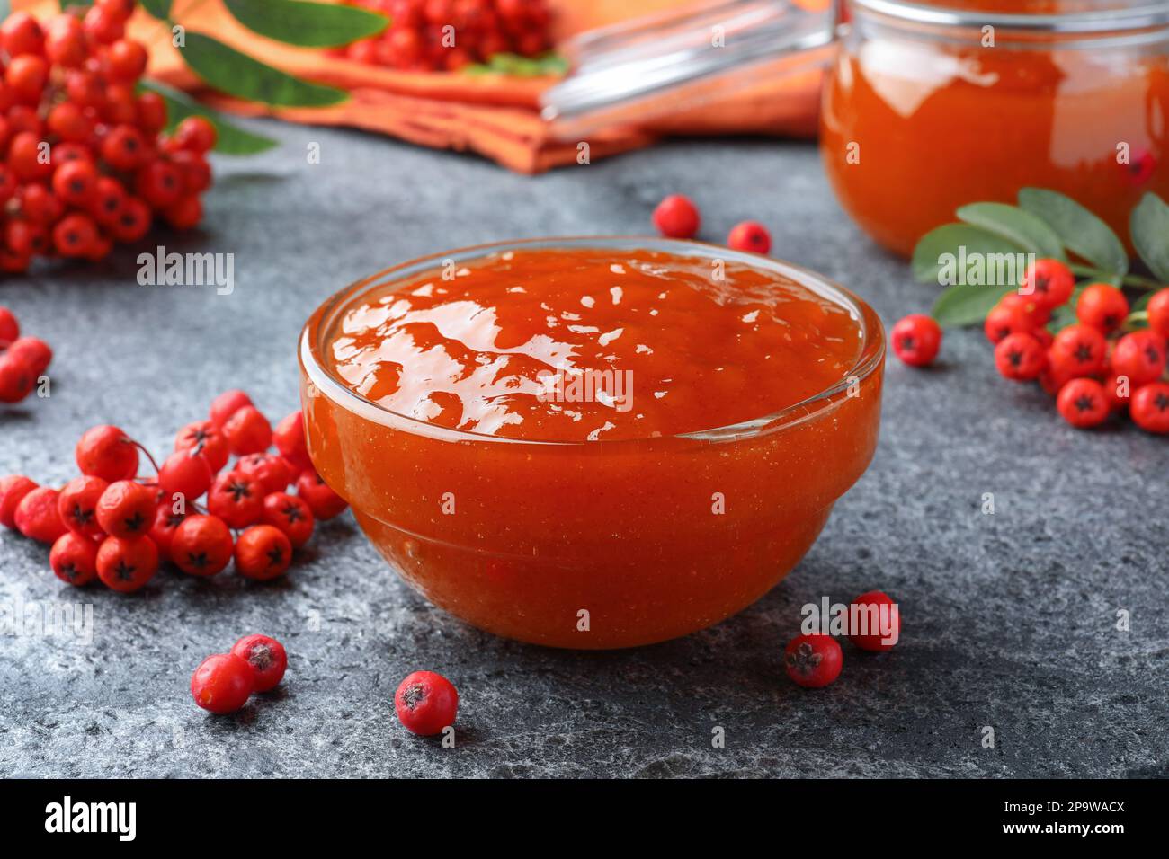 Delicious rowan jam in glass bowl and berries on grey table, closeup Stock Photo