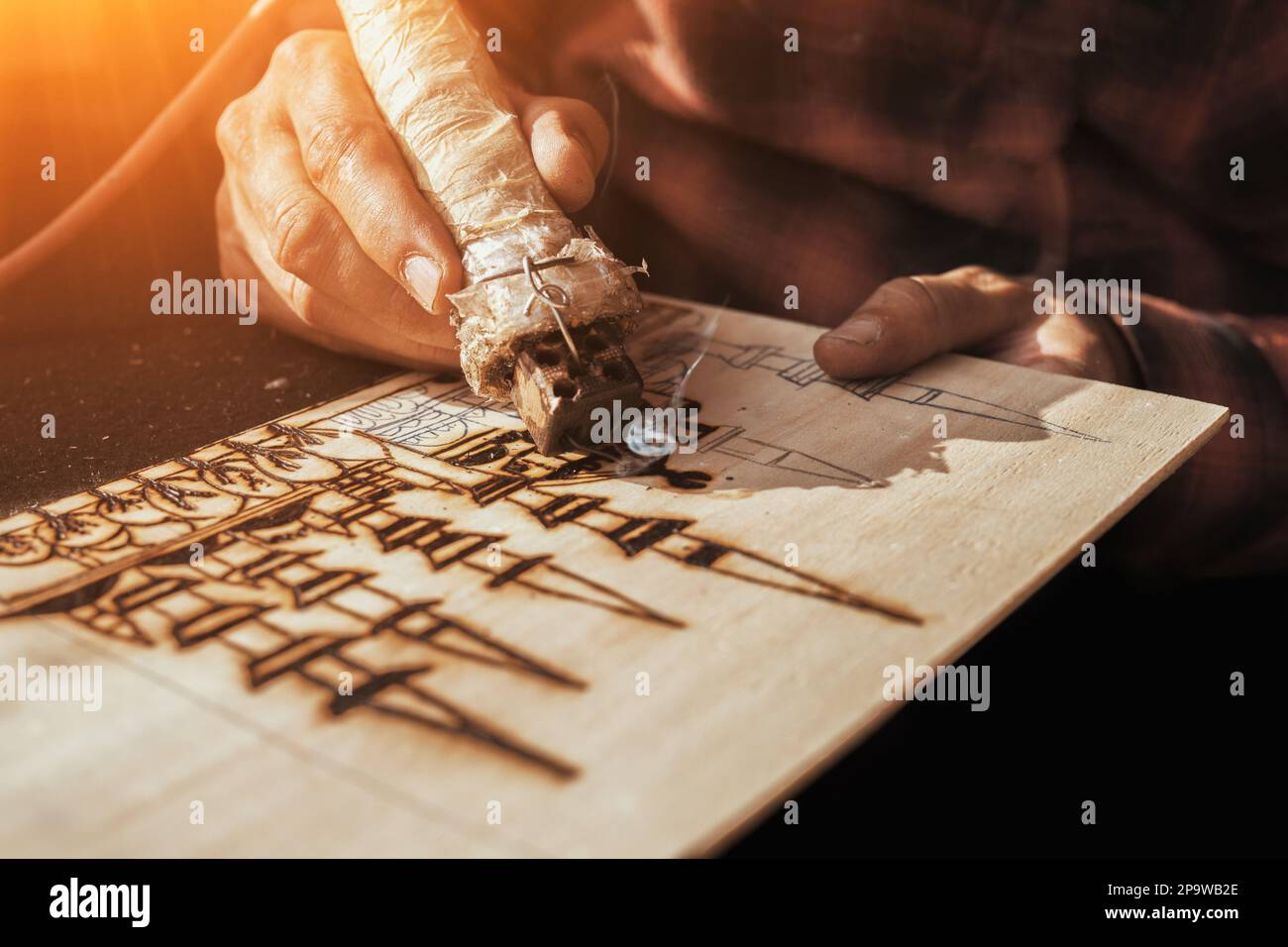 An artist using a pyrography tool to create a pyrogravure. Wood burning with pyrography pen. Stock Photo
